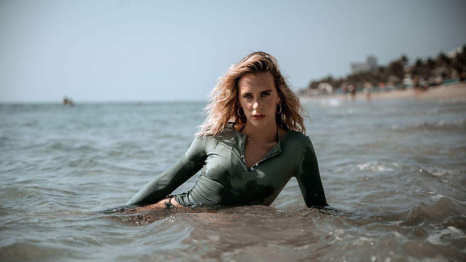 Person in green shirt lying in ocean waves at beach during moody weather.