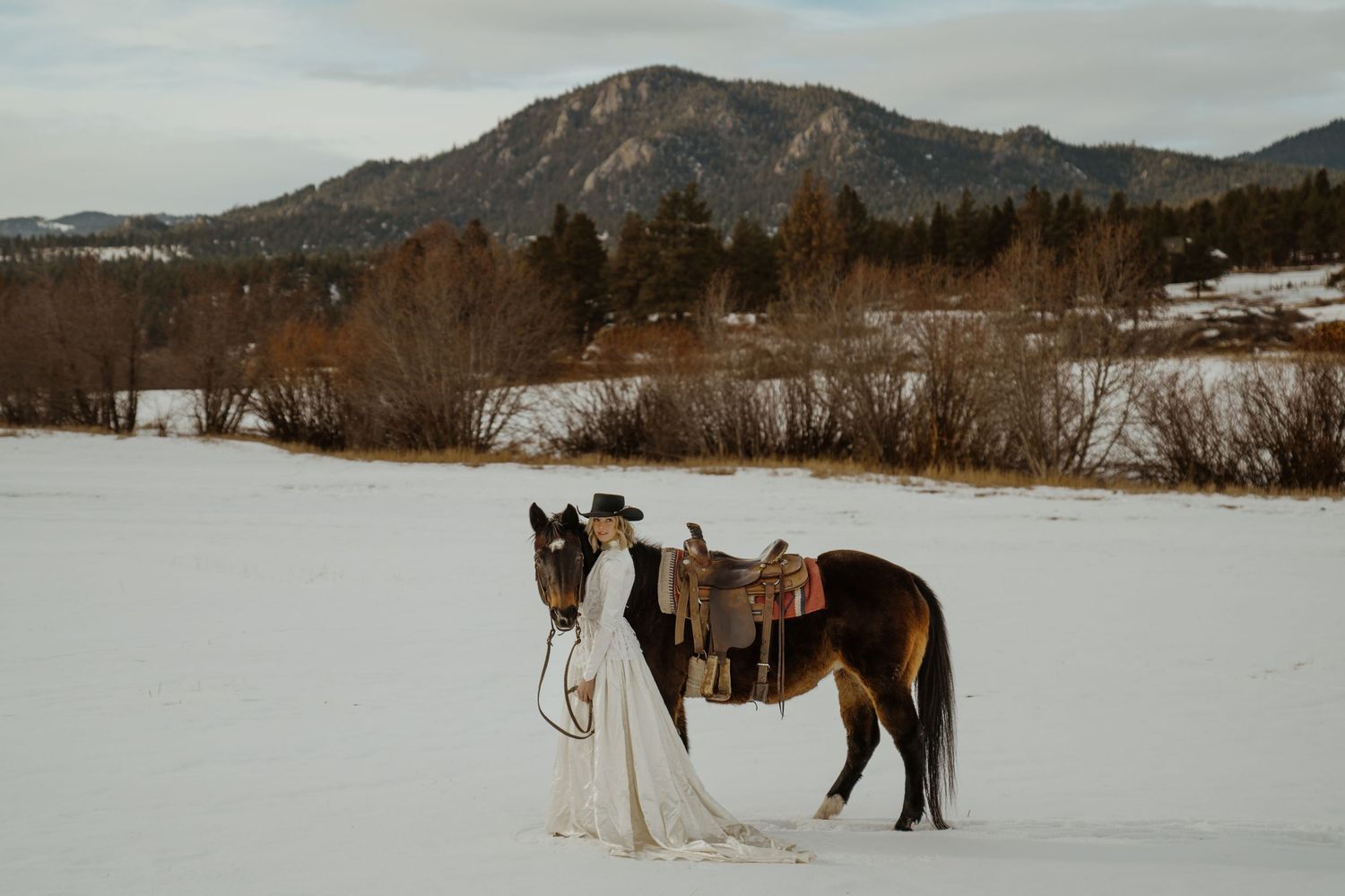 Western style winter bridal photos showing snowy mountain landscapes and a bride in a vintage wedding gown posed next to her horse.