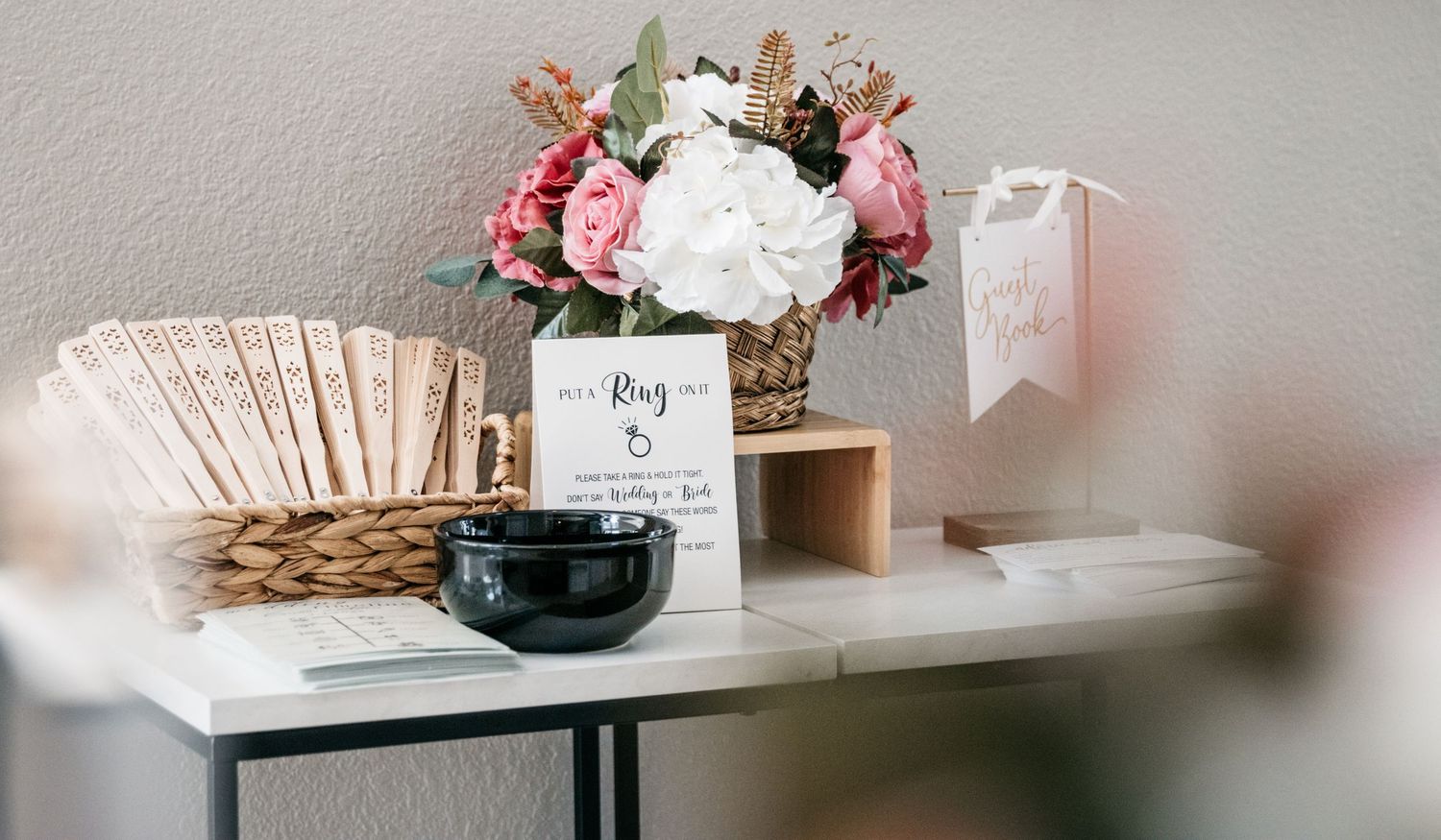 A modern table display with a black bowl, delicate floral arrangement in pink and white, and paper items in neutral tones.