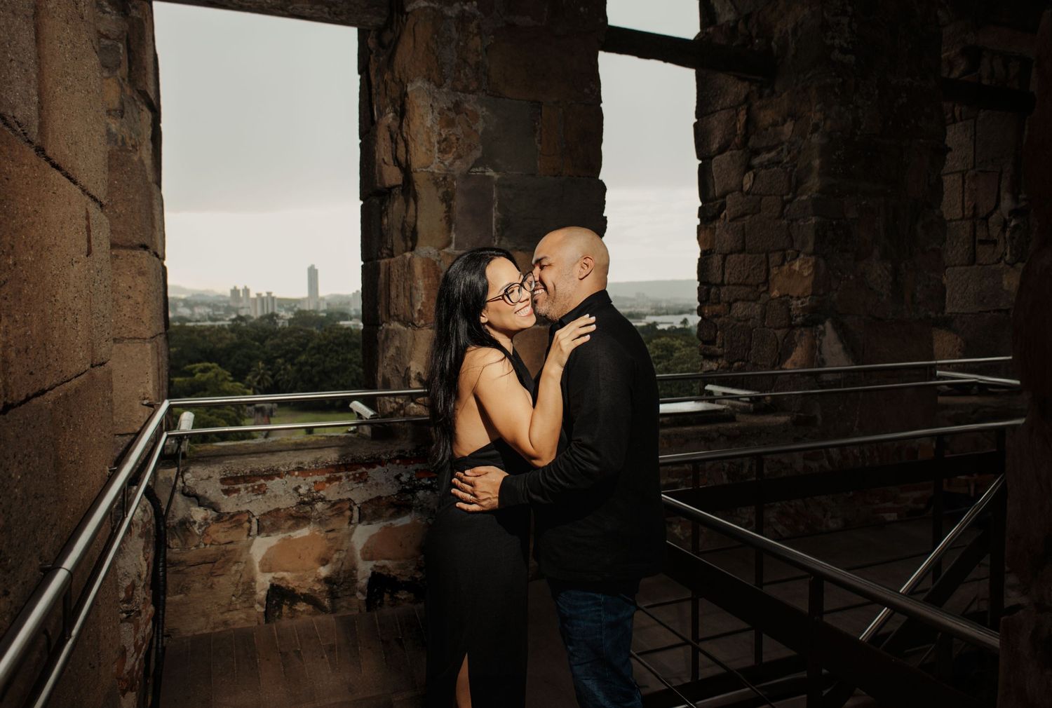 Couple shares romantic moment in historic stone architecture with city view.