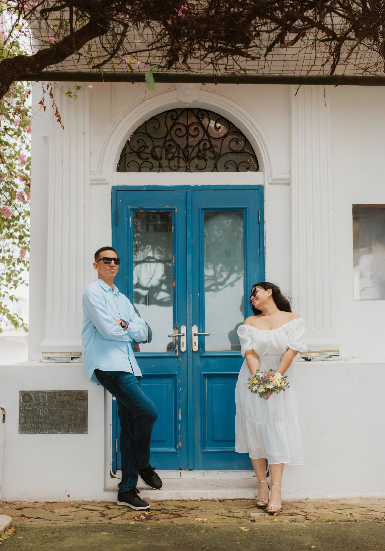 Stylish couple posing by vintage blue doors of white building.