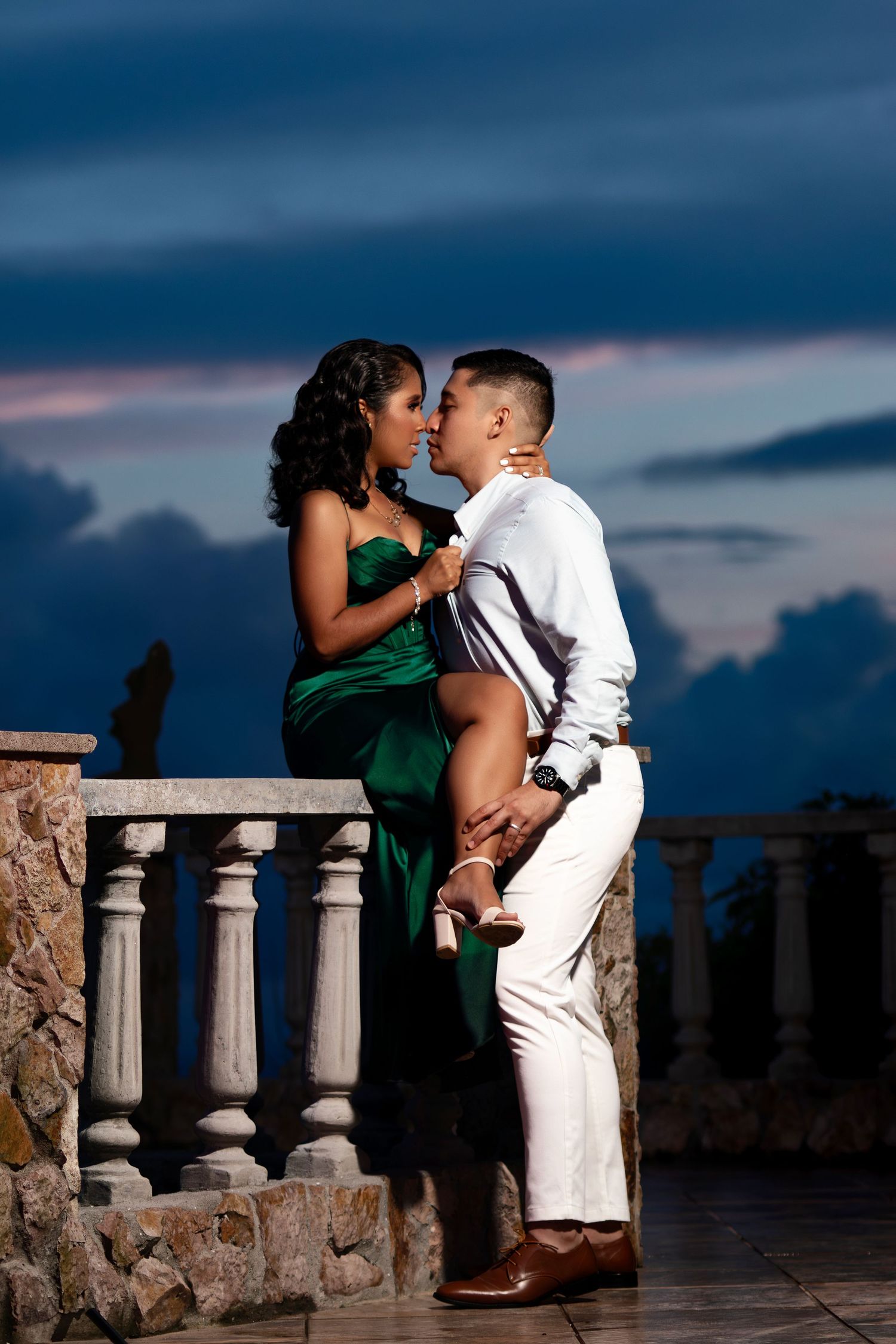 Intimate moment between couple in formal wear on mountainside balcony at dusk.