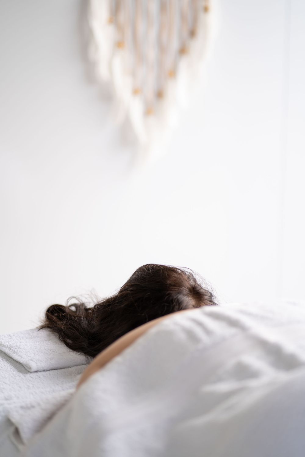Person resting on white pillow with decorative heart hanging on wall in background.