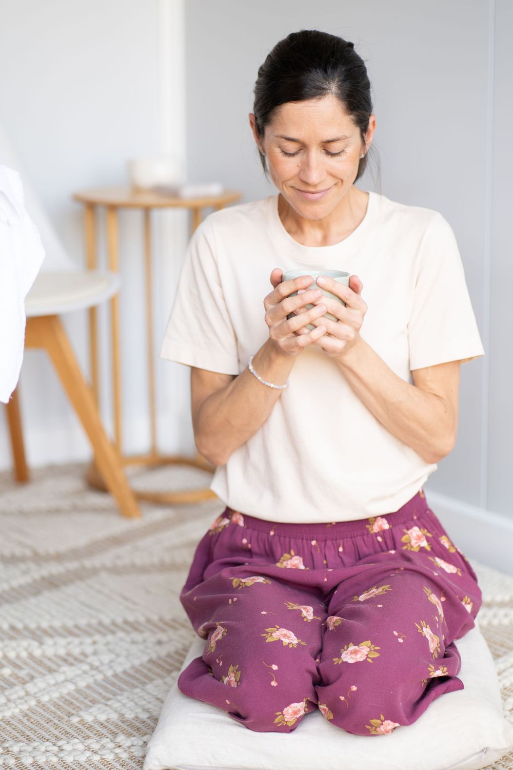 Person in white t-shirt and purple patterned pants kneeling peacefully with a cup in their hands.