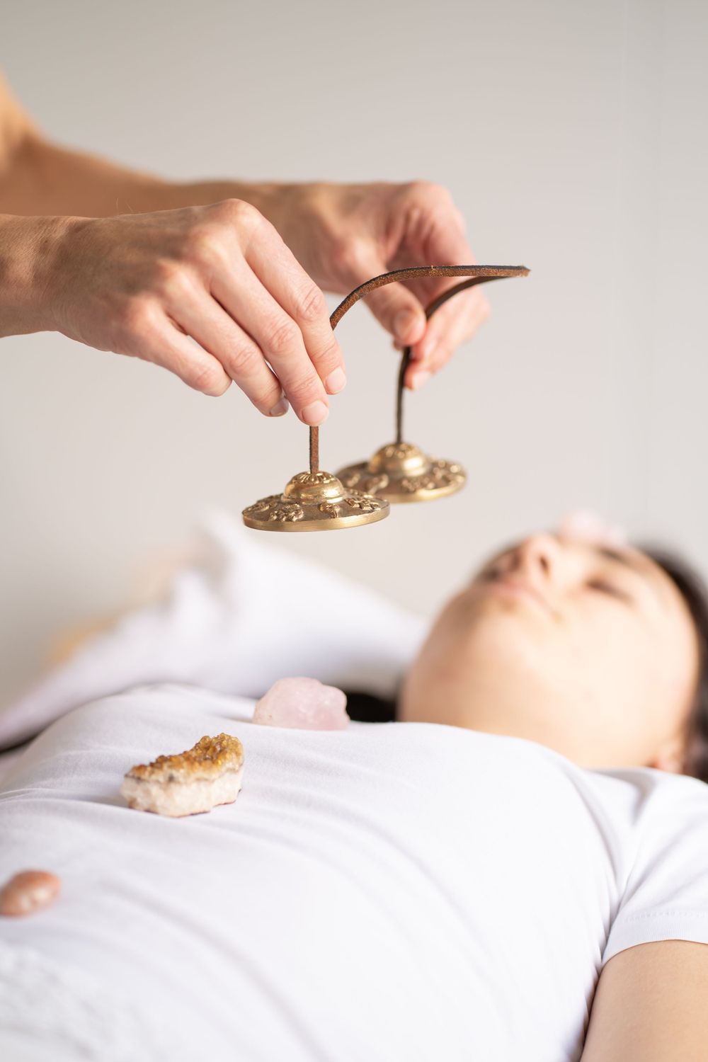 Crystal healing session showing hands holding stones over reclining person in white.