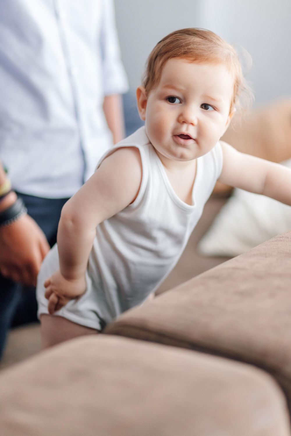 Baby in white onesie smiling while sitting on couch.