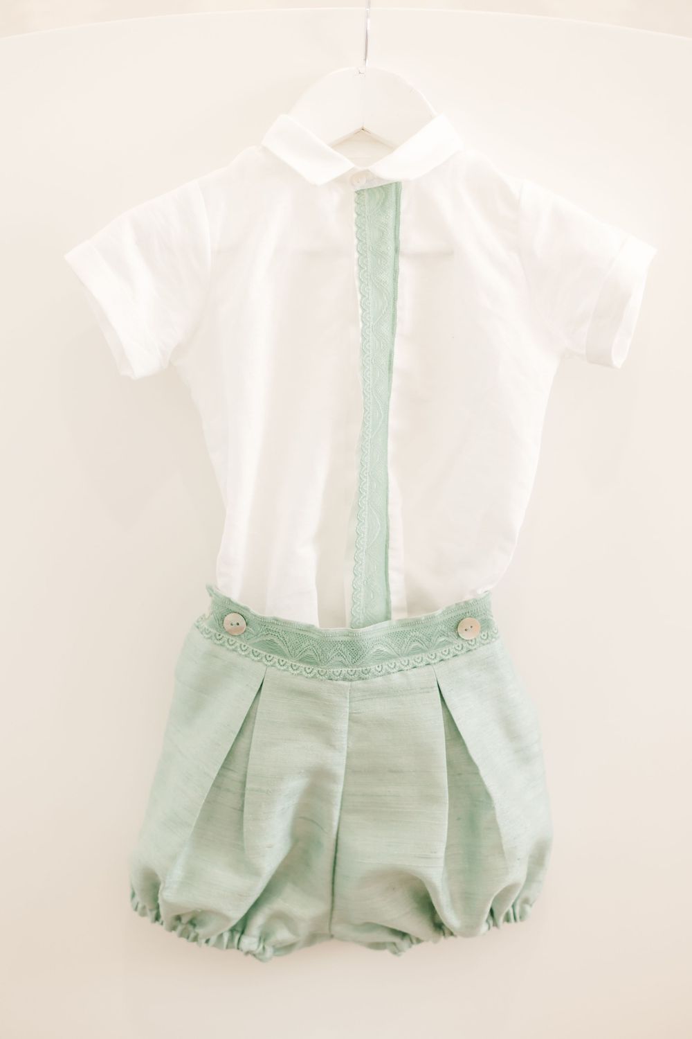 Vintage-style baby outfit with white shirt and mint green bloomers hanging on display.