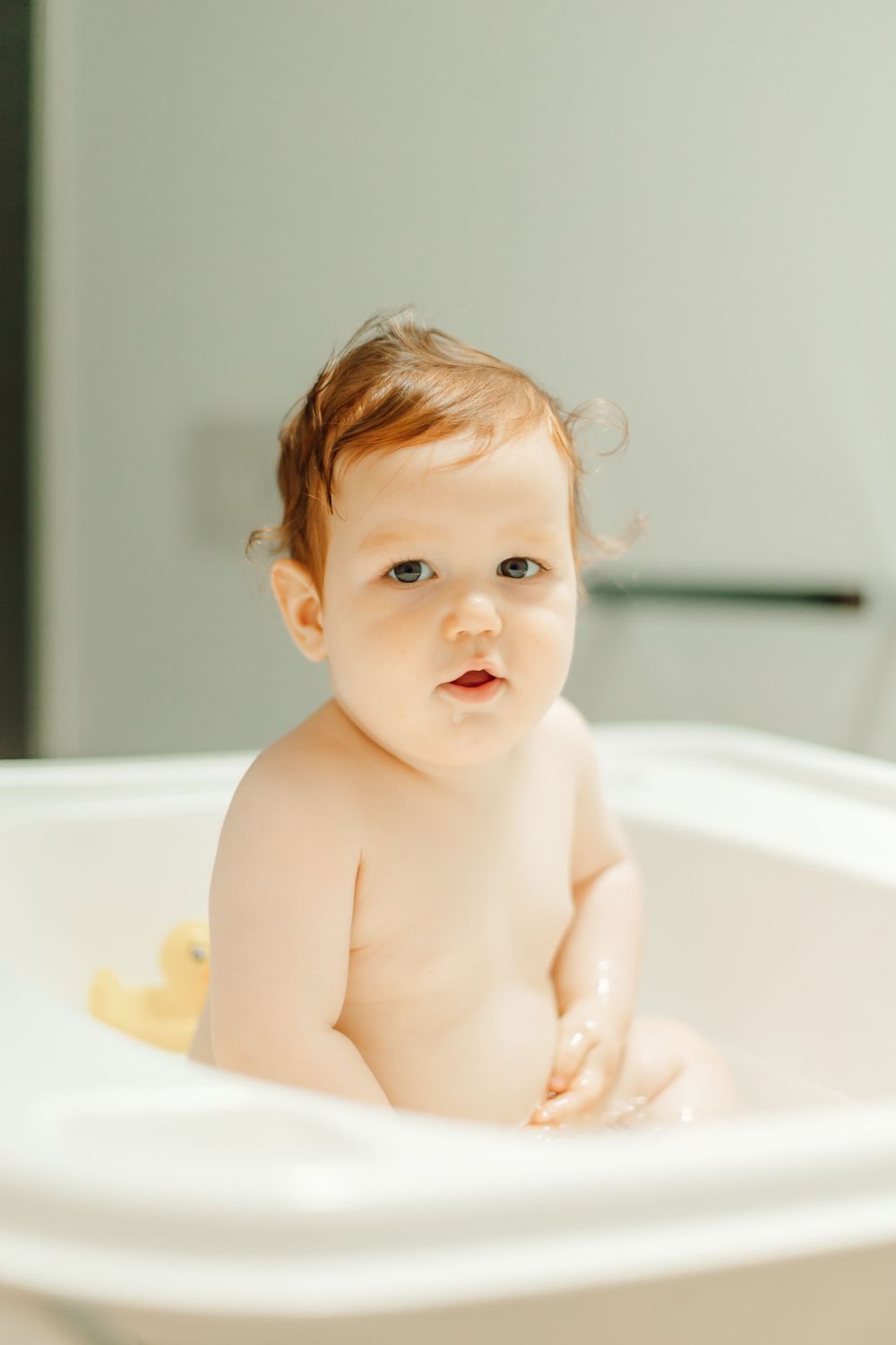A small baby sits in a white bathtub during bathtime.
