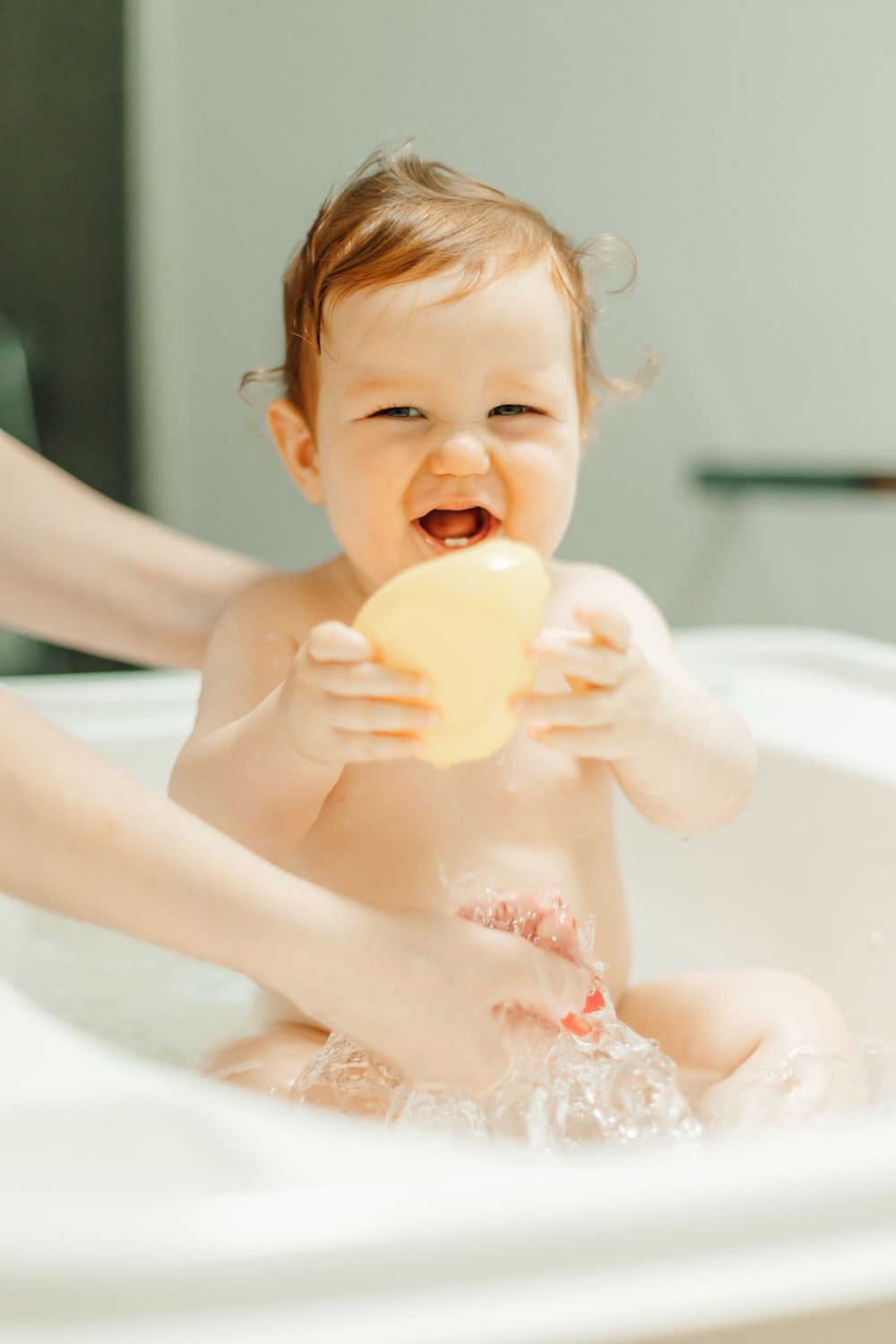 Baby playing with yellow rubber duck during bath time.