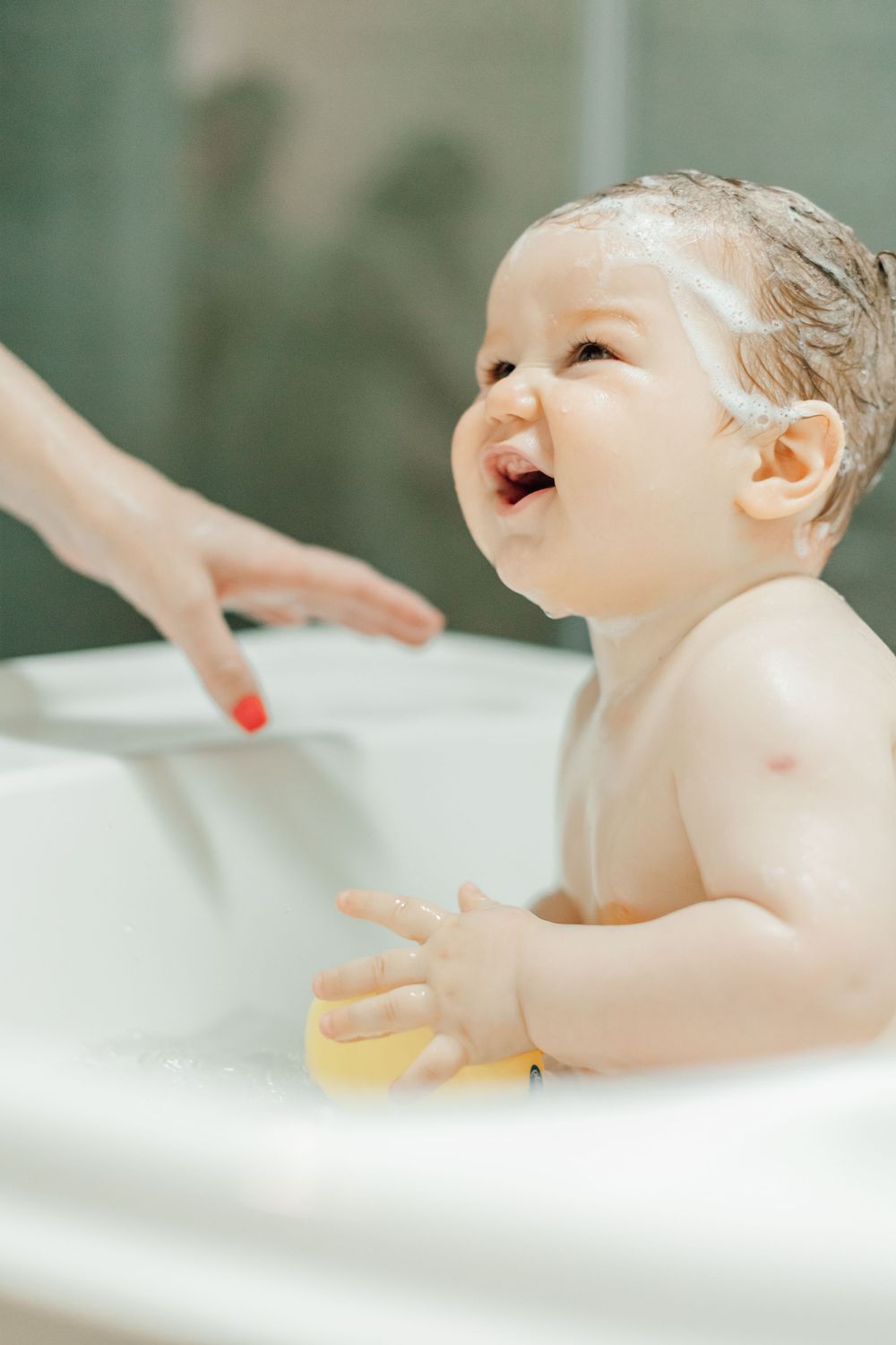 Joyful bathtime moment captured as baby plays in white bathtub.