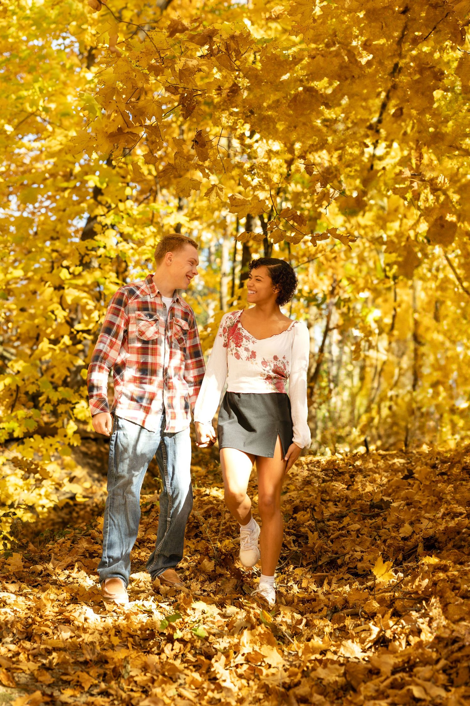 A couple walks together on a path surrounded by vibrant golden fall foliage.