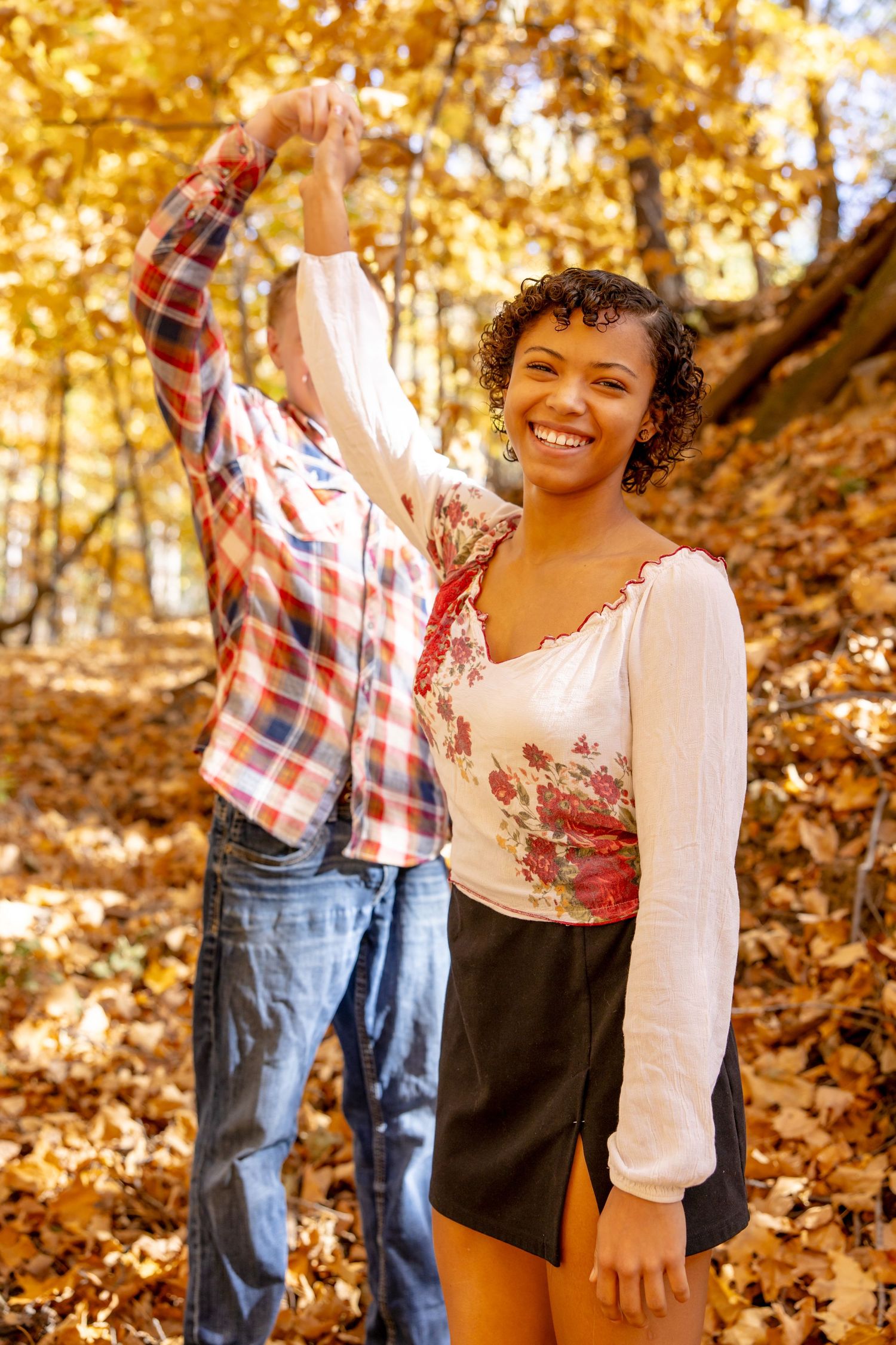 A couple dances joyfully among fallen autumn leaves and golden trees.