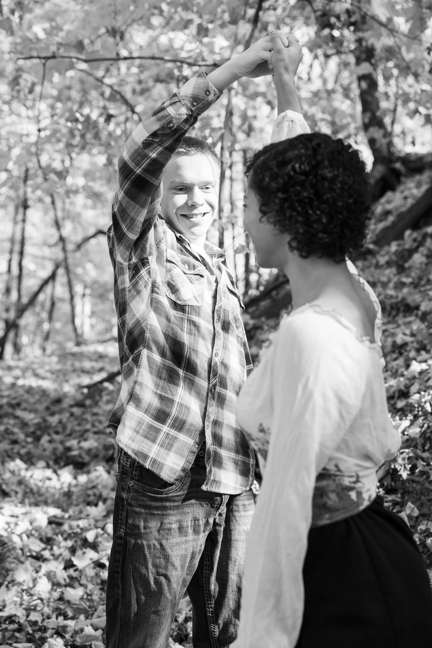 A couple dances together in black and white against a backdrop of trees.