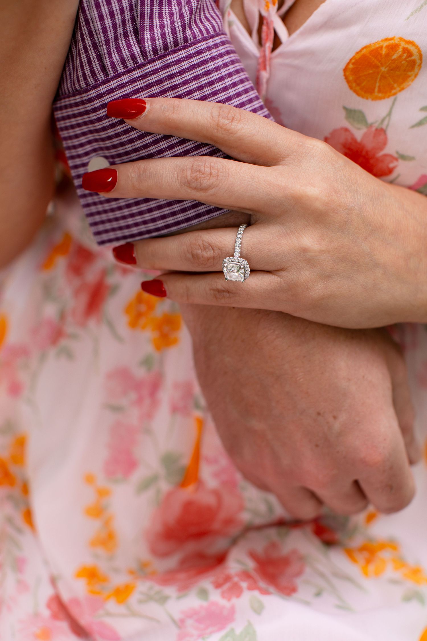 Close-up view of hands with a sparkling diamond engagement ring against a floral patterned background.