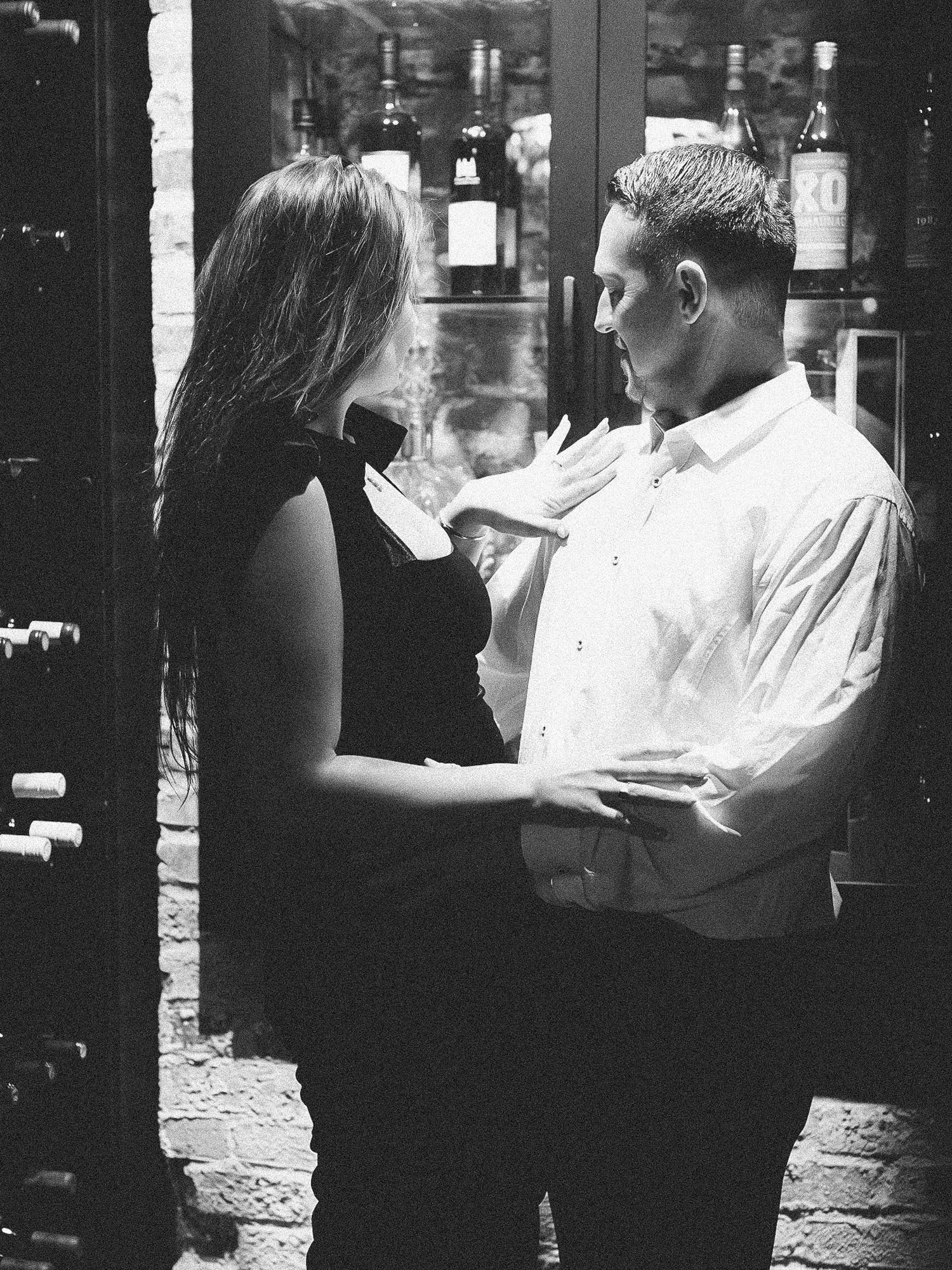 A romantic black and white moment between a couple in an intimate setting with wine bottles in the background.