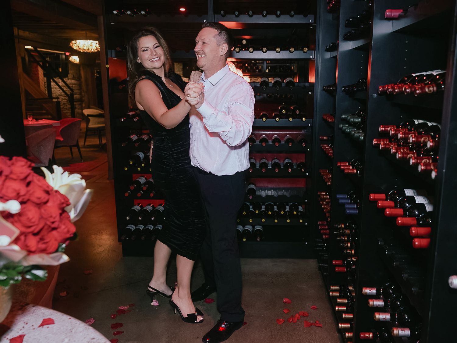 Dancers move gracefully across a dark room with wine storage and red lighting accents.