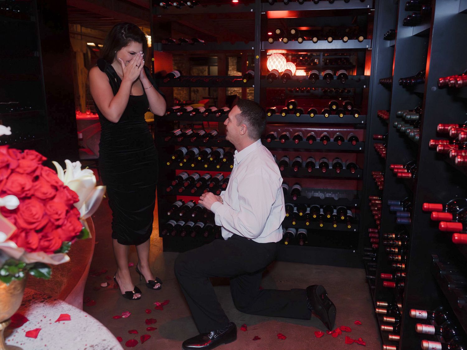 A romantic proposal scene in a dimly lit venue with red lighting and decorative elements.
