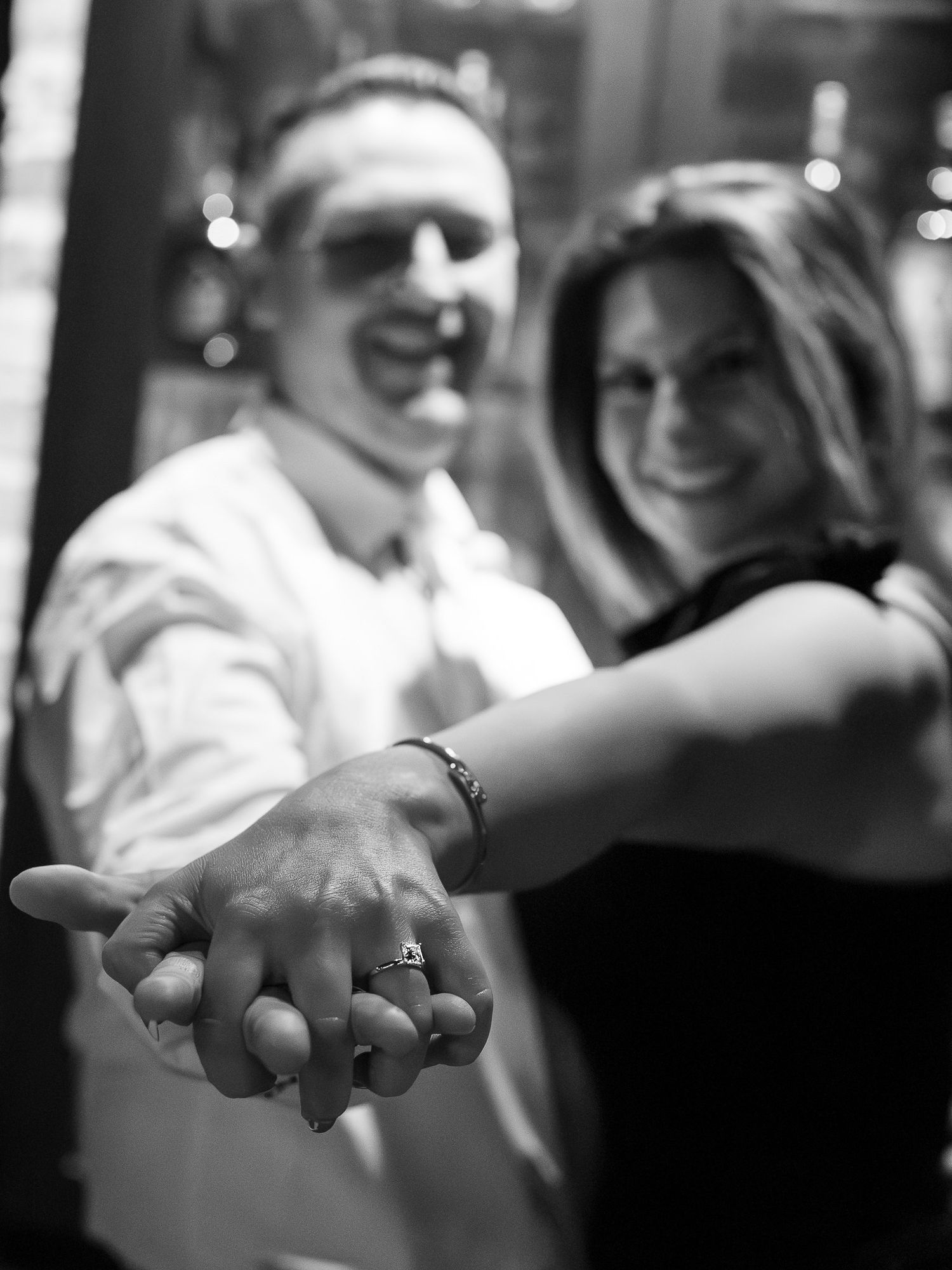 Black and white engagement photo showing couple holding hands with engagement ring in focus.
