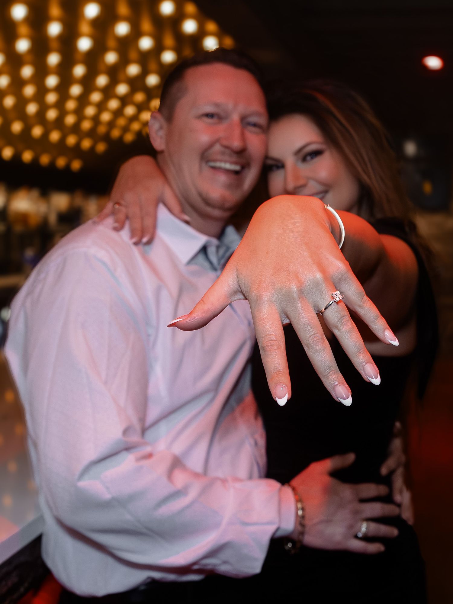 A close-up shot of hands showing off an engagement ring in a romantic evening setting.