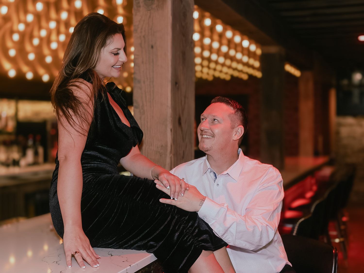 A couple shares an intimate dance moment under warm string lights at an indoor venue.