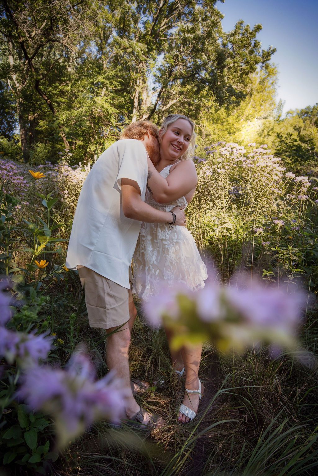 Sweet moment captured in flowering meadow with sunlit trees in background.