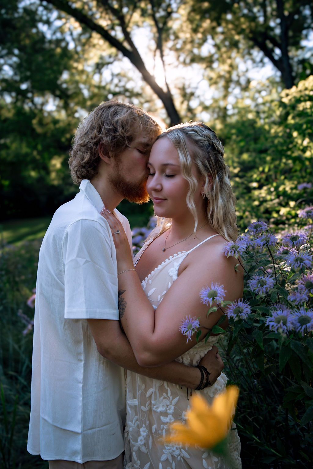 Intimate moment between couple surrounded by blooming flowers in natural outdoor setting.