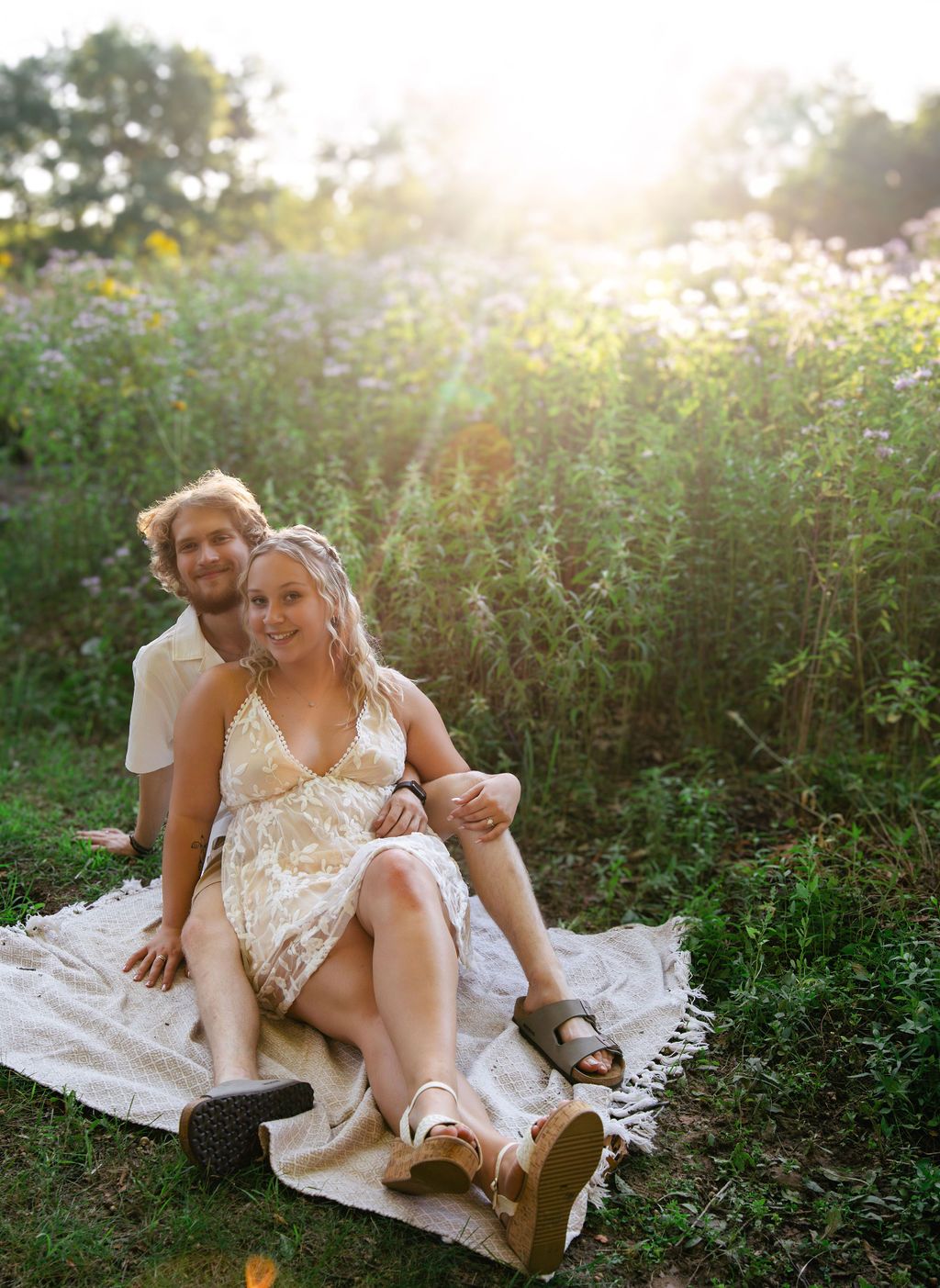Couple lounging together on a white blanket in a wildflower meadow at sunset.