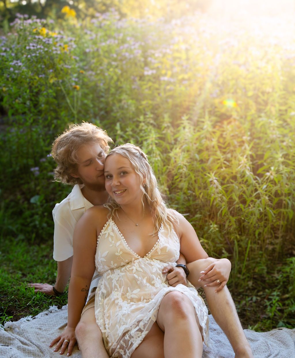 Sweet couple sharing tender moments on white blanket in sunlit meadow.