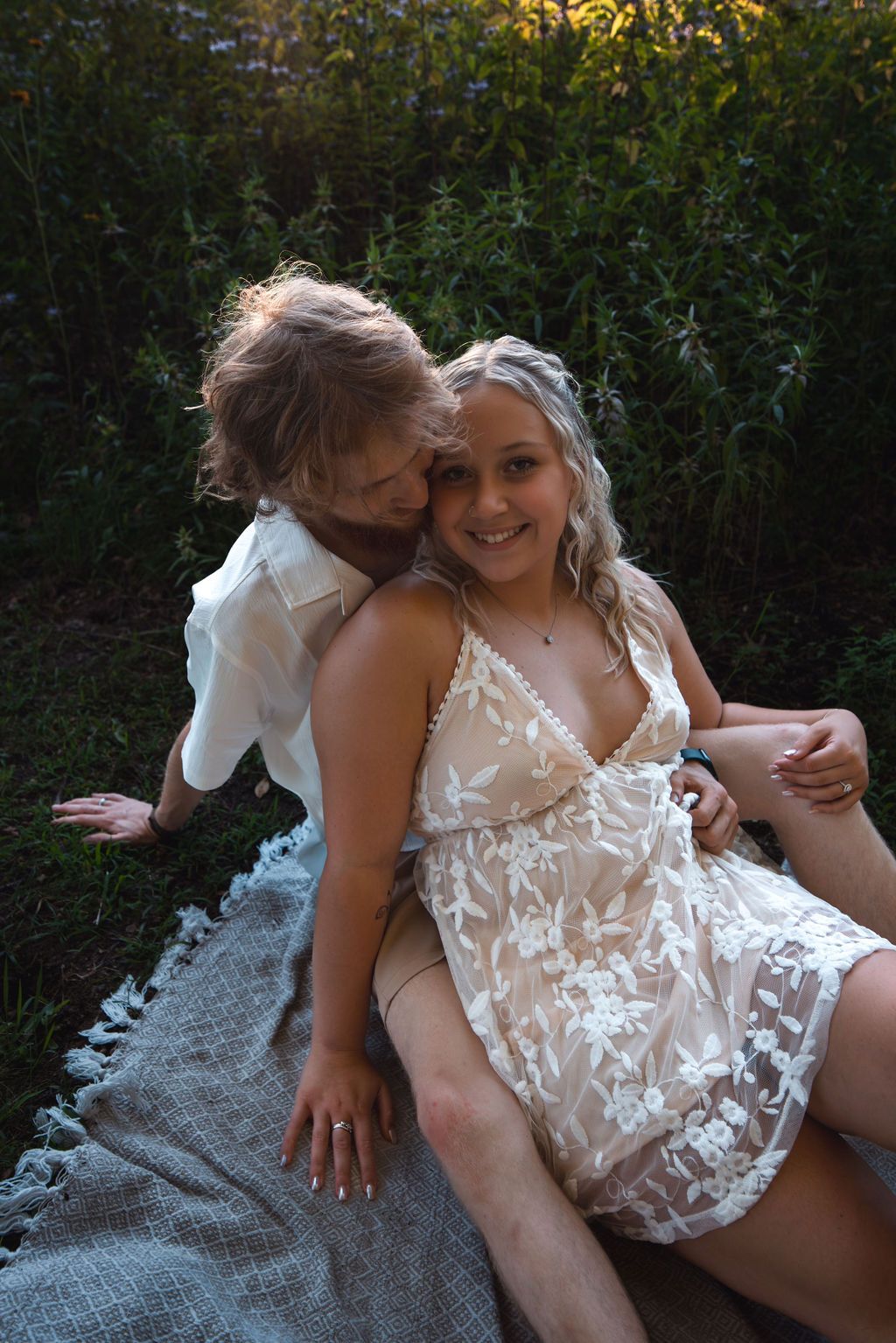 Playful couple sharing intimate moments on blanket surrounded by nature.
