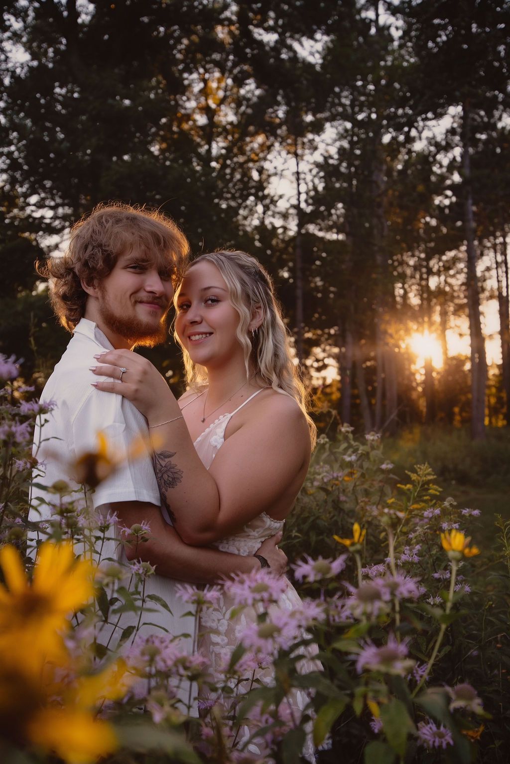 Couple sharing romantic moment among wildflowers at sunset in wooded area.