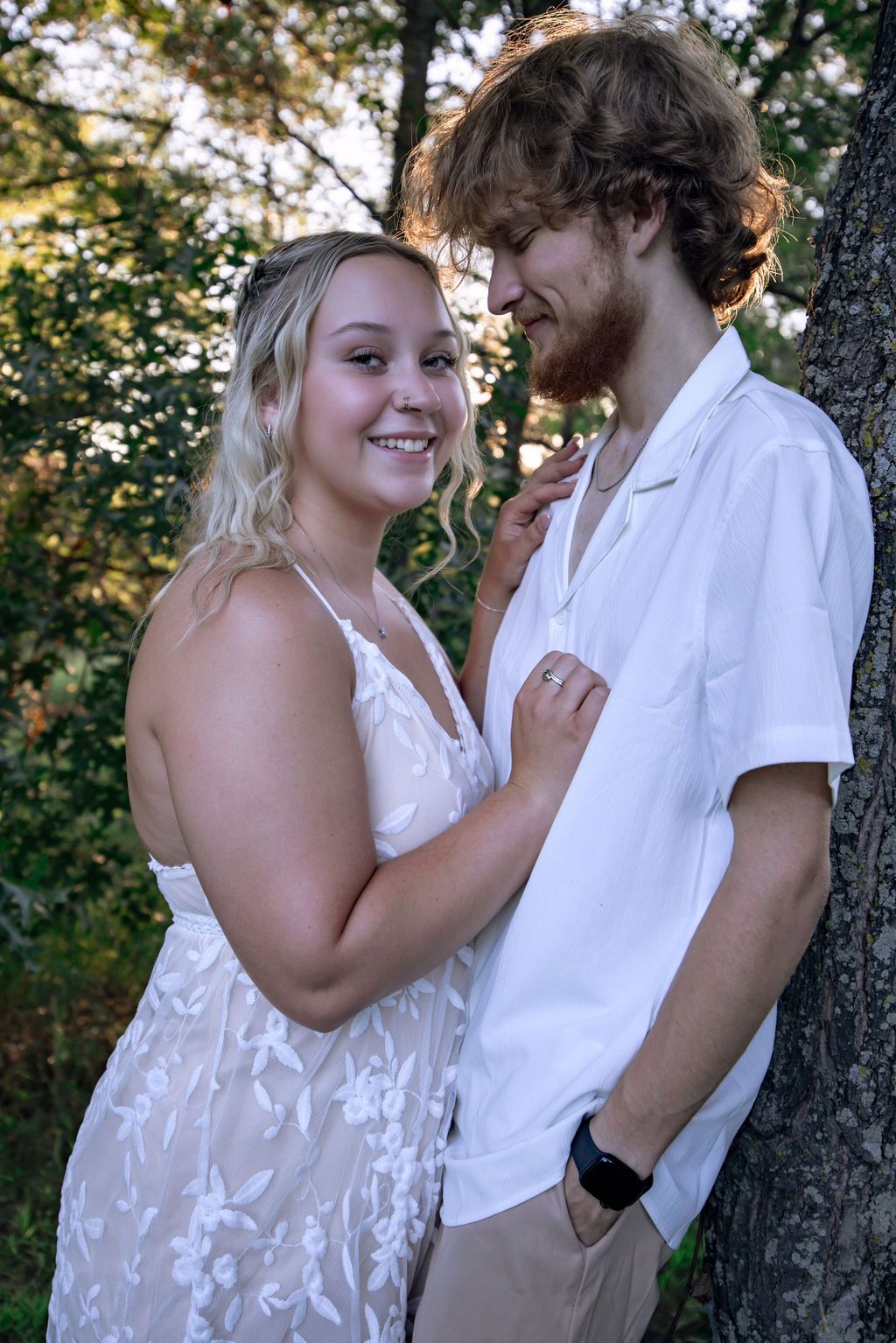 Couple sharing playful moment against tree in outdoor garden setting.