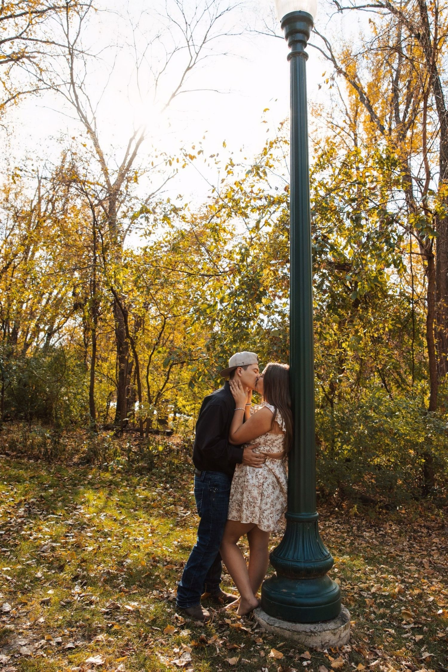 Romantic autumn scene with couple embracing by vintage lamppost surrounded by falling leaves.