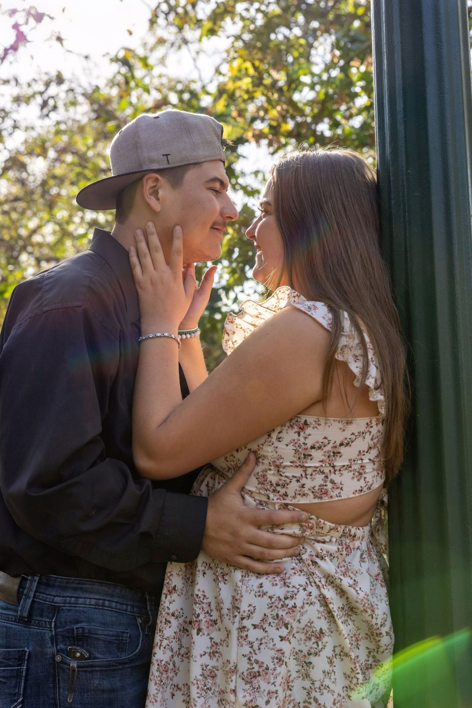 Romantic couple sharing an intimate moment in golden sunlight by a green lamppost.