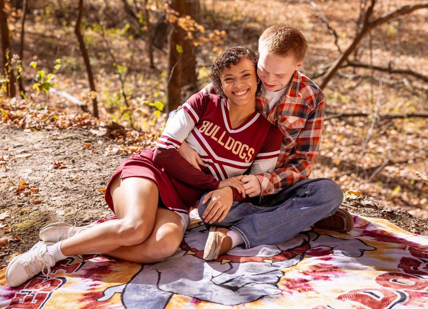 A couple sits together on a floral blanket having a picnic in the autumn woods.