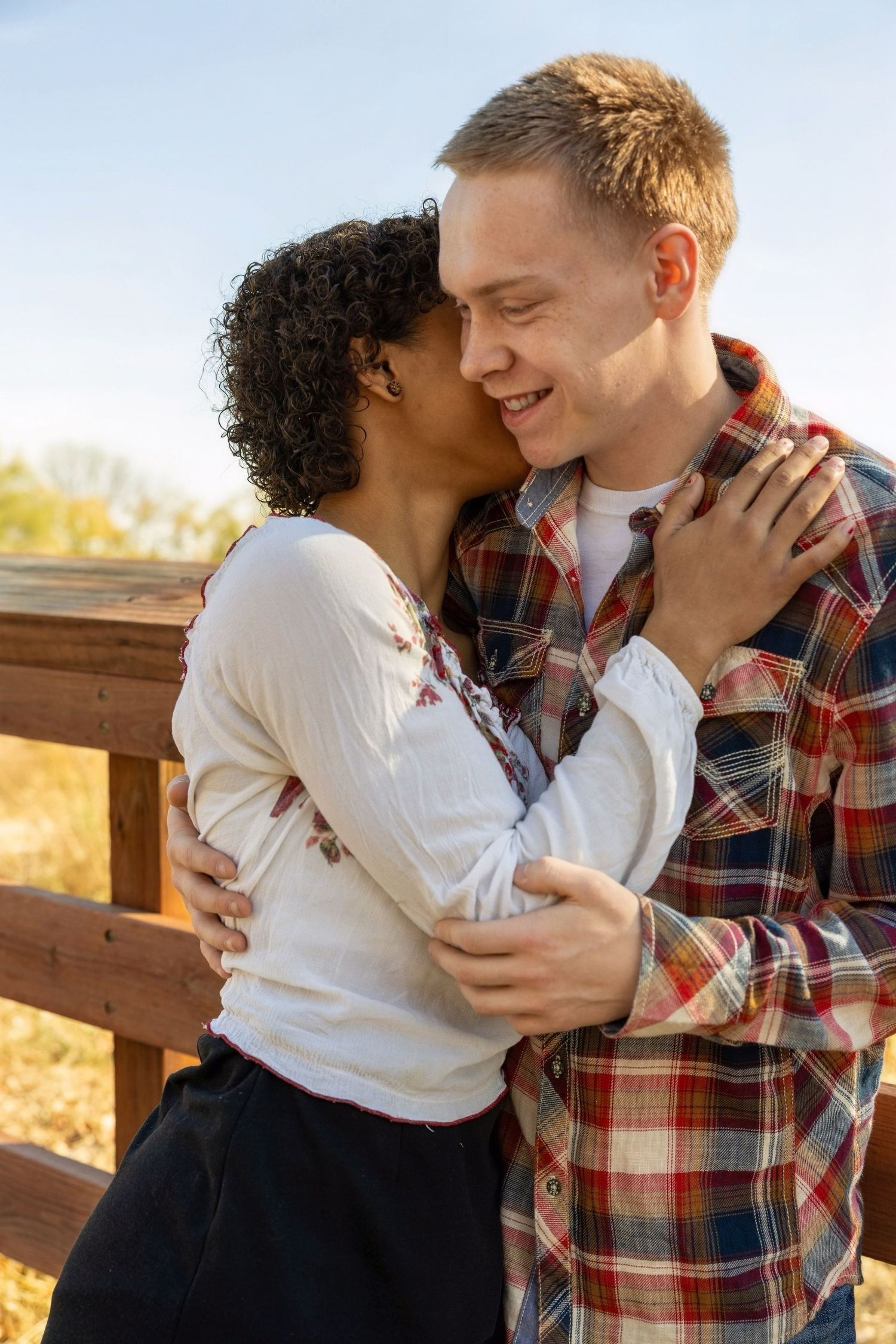 A romantic couple embraces on a wooden deck during sunset with autumn scenery in the background.