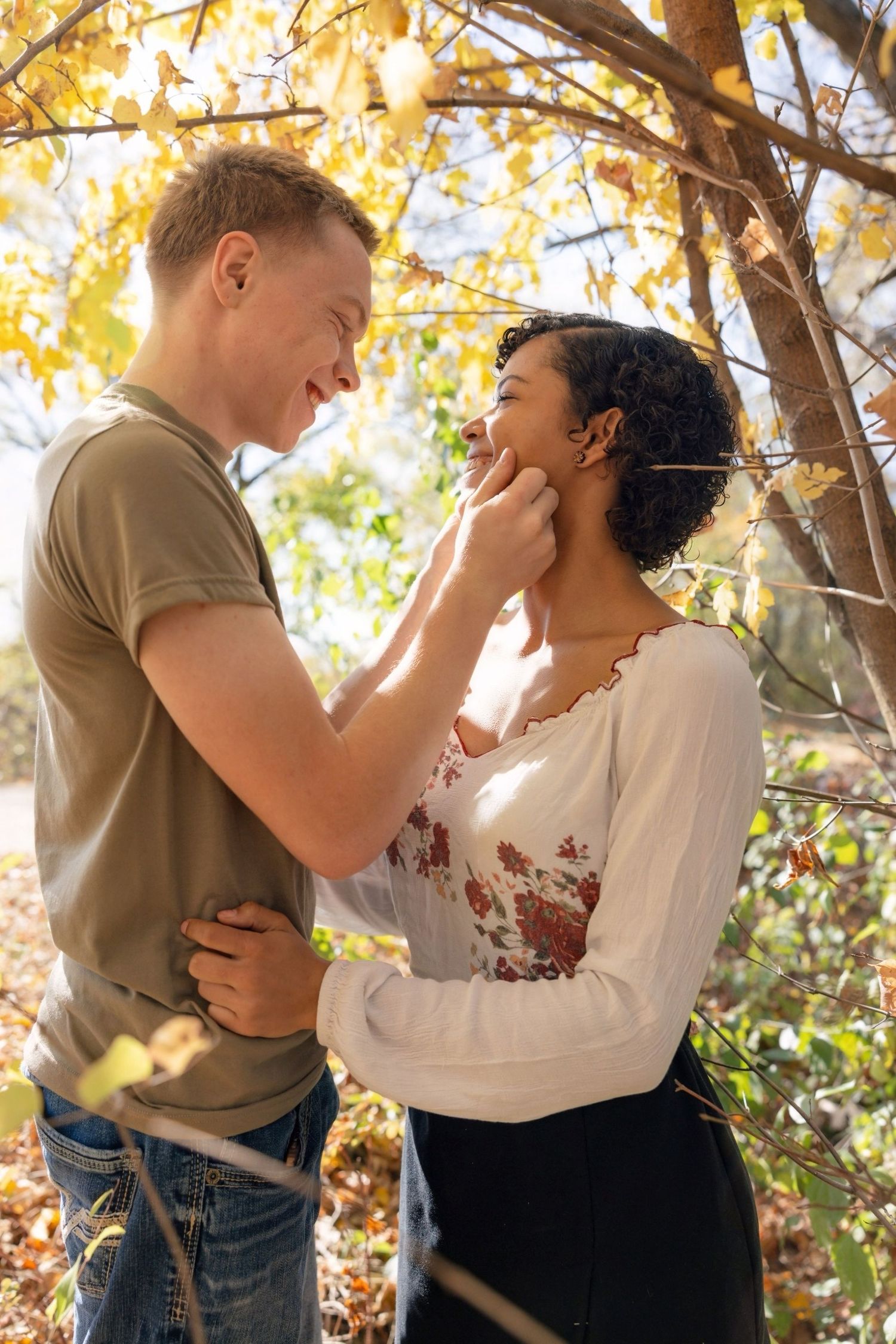 A couple shares an intimate moment beneath golden autumn tree branches.