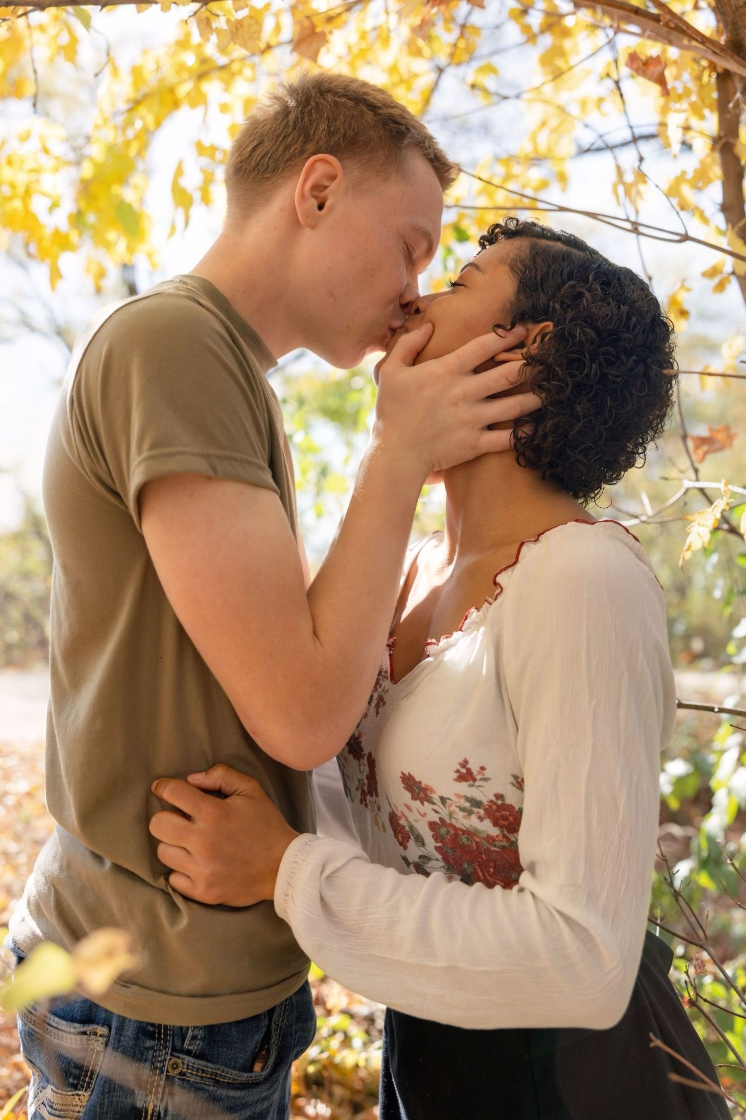 A romantic couple embraces in an intimate moment surrounded by golden fall foliage.