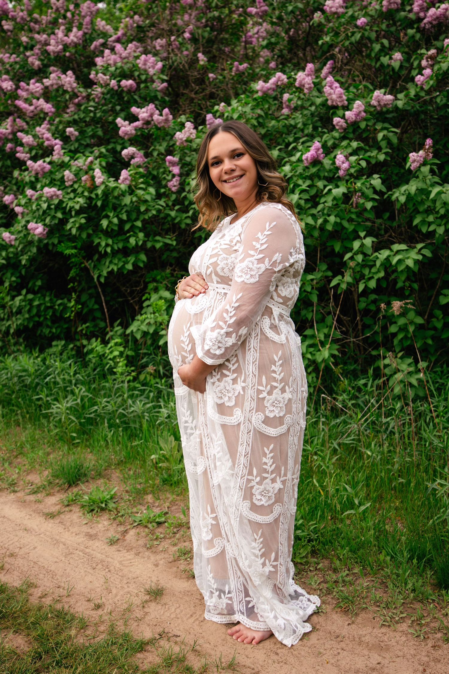 A lace maternity gown photoshoot in a garden with blooming pink flowers and natural outdoor setting.