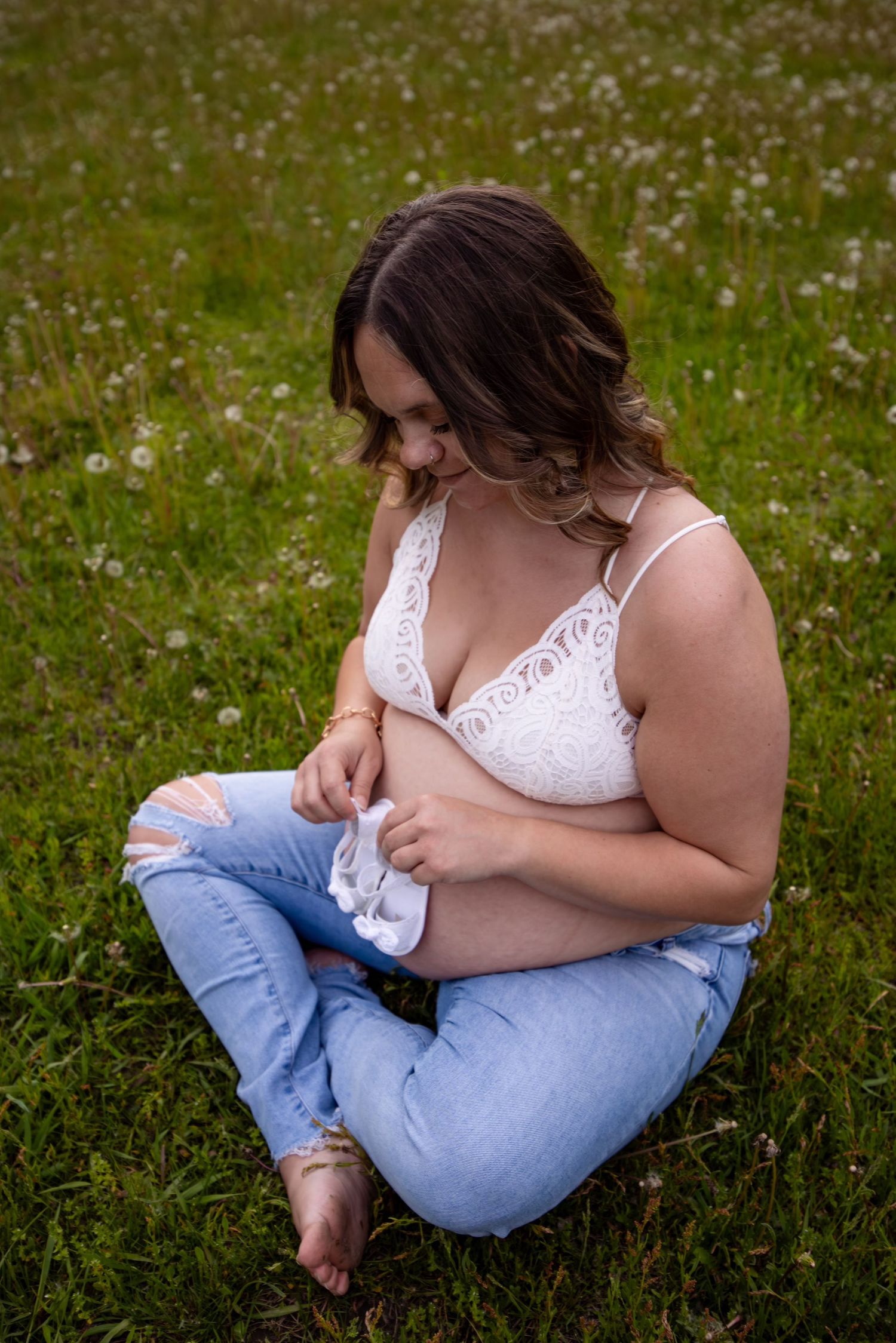 Person sitting in a wildflower meadow wearing blue jeans and white top looking down thoughtfully on a summer day.