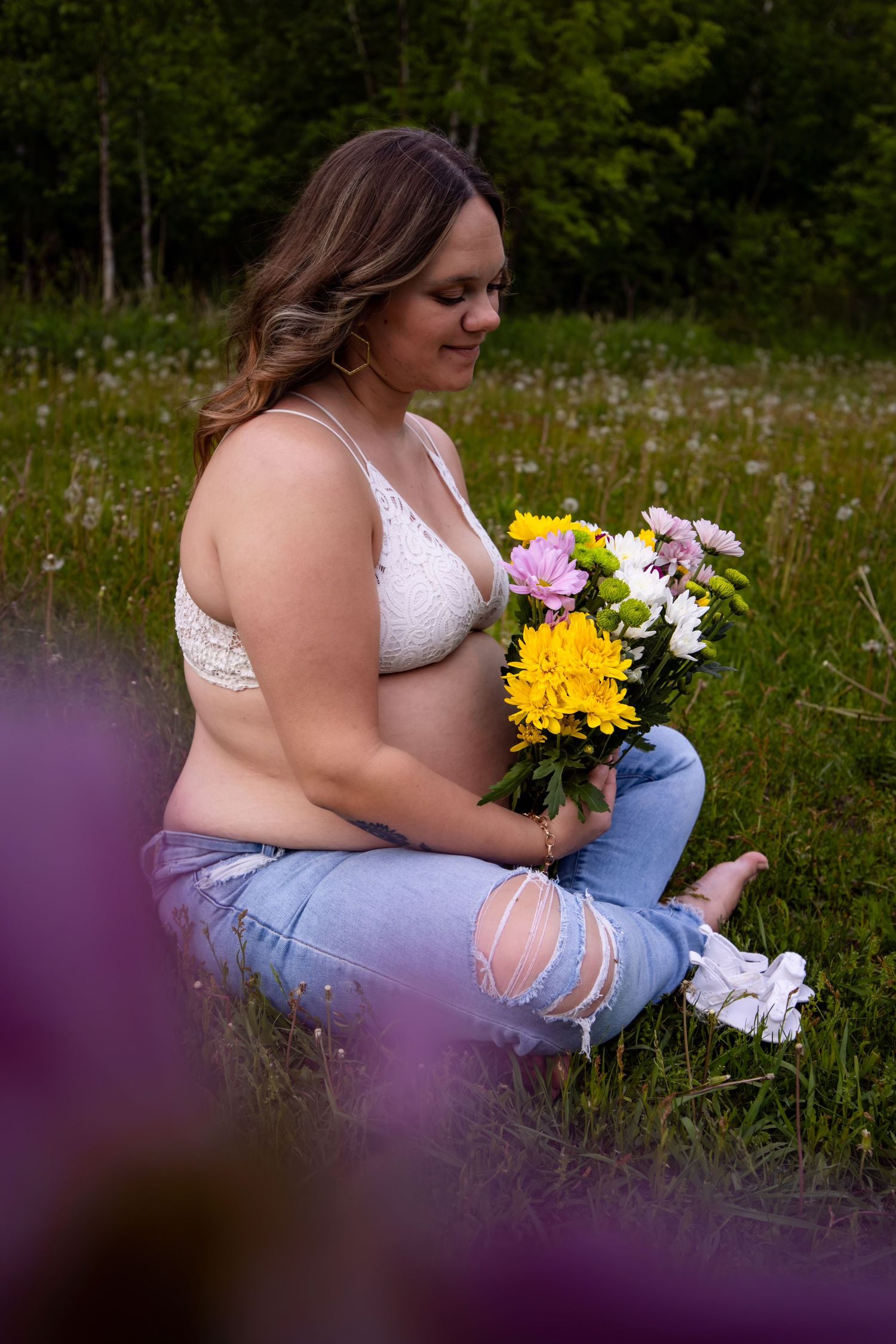Person in white top and jeans sits in wildflower field holding colorful bouquet at sunset.