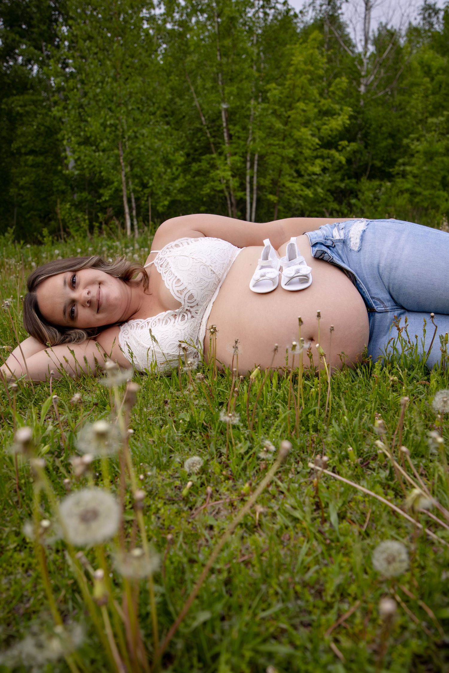 Person lying in grass field surrounded by dandelions wearing white top and jeans.