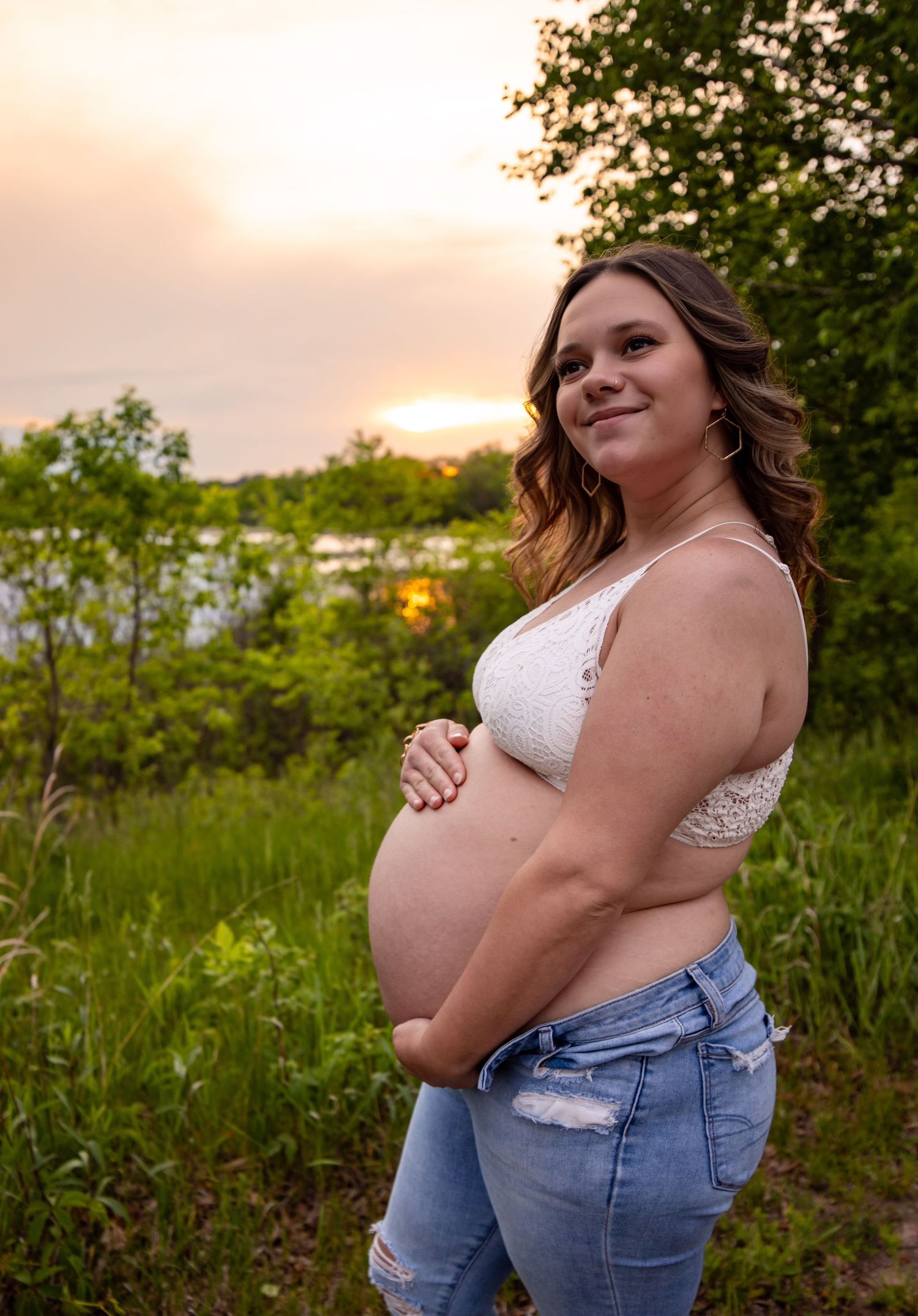 A maternity photo taken at sunset showing a pregnant figure in white lace top and jeans.