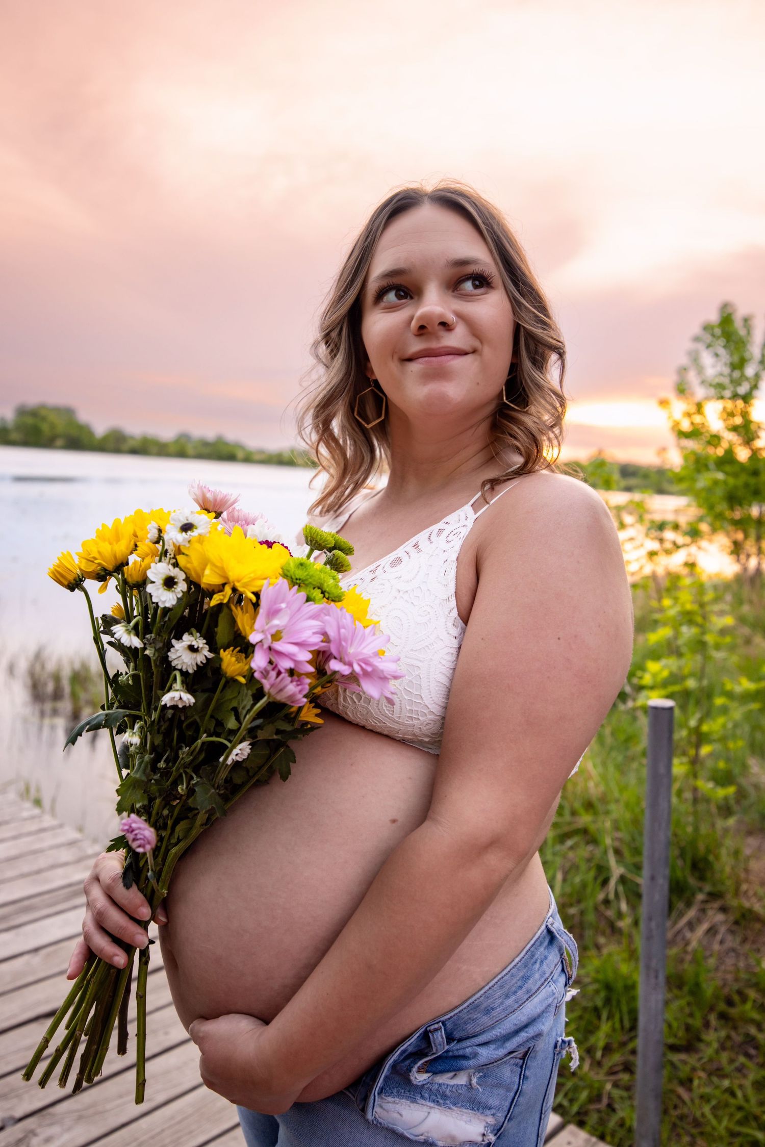 Sunset maternity portrait with person holding colorful flower bouquet on wooden deck.