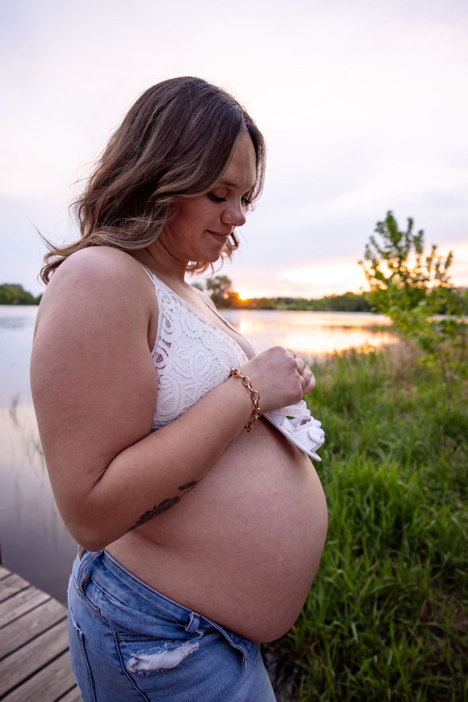 Sunset maternity photoshoot on a wooden dock by the water with natural lighting.