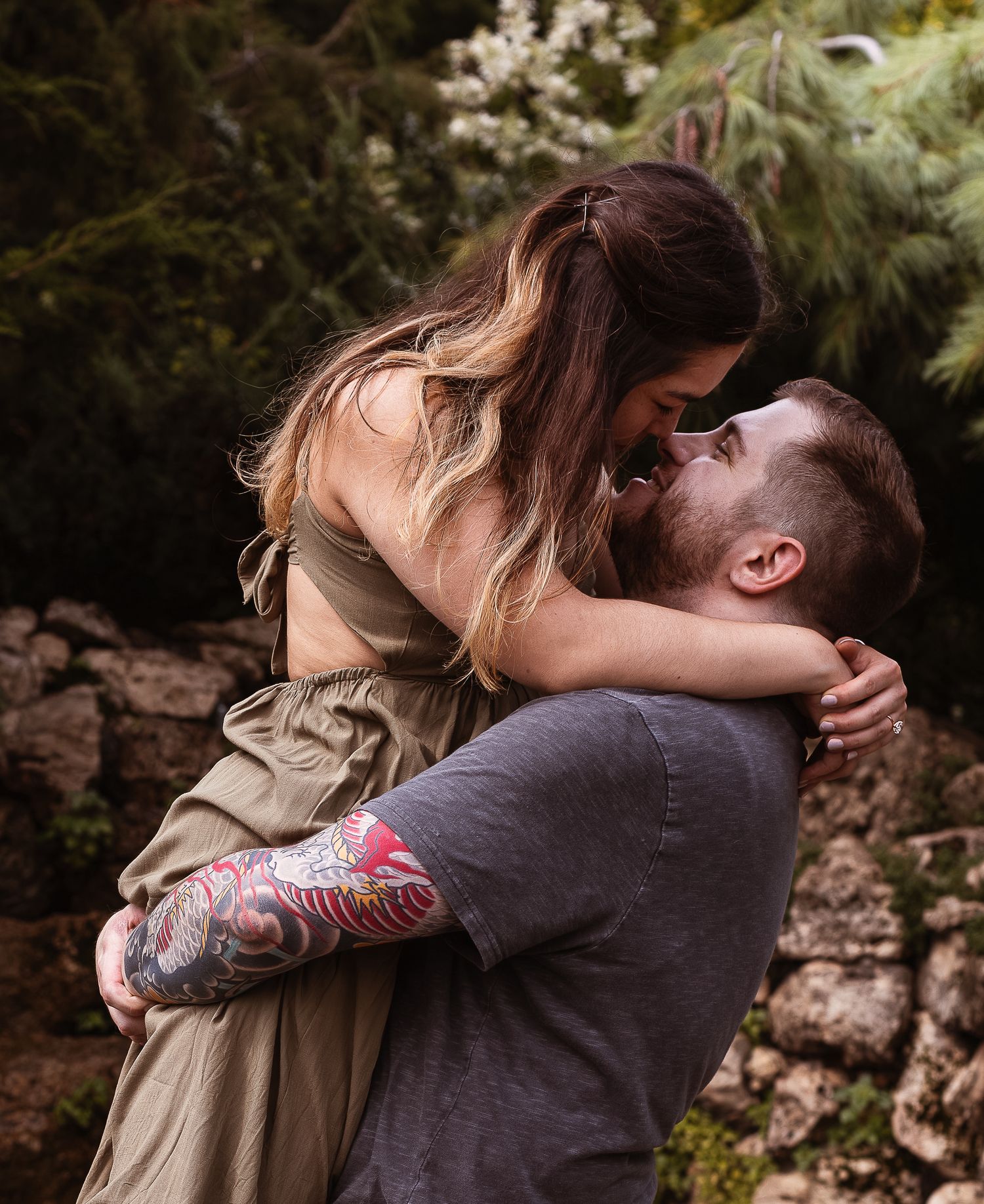 A couple embracing and kissing in a natural outdoor forest setting.