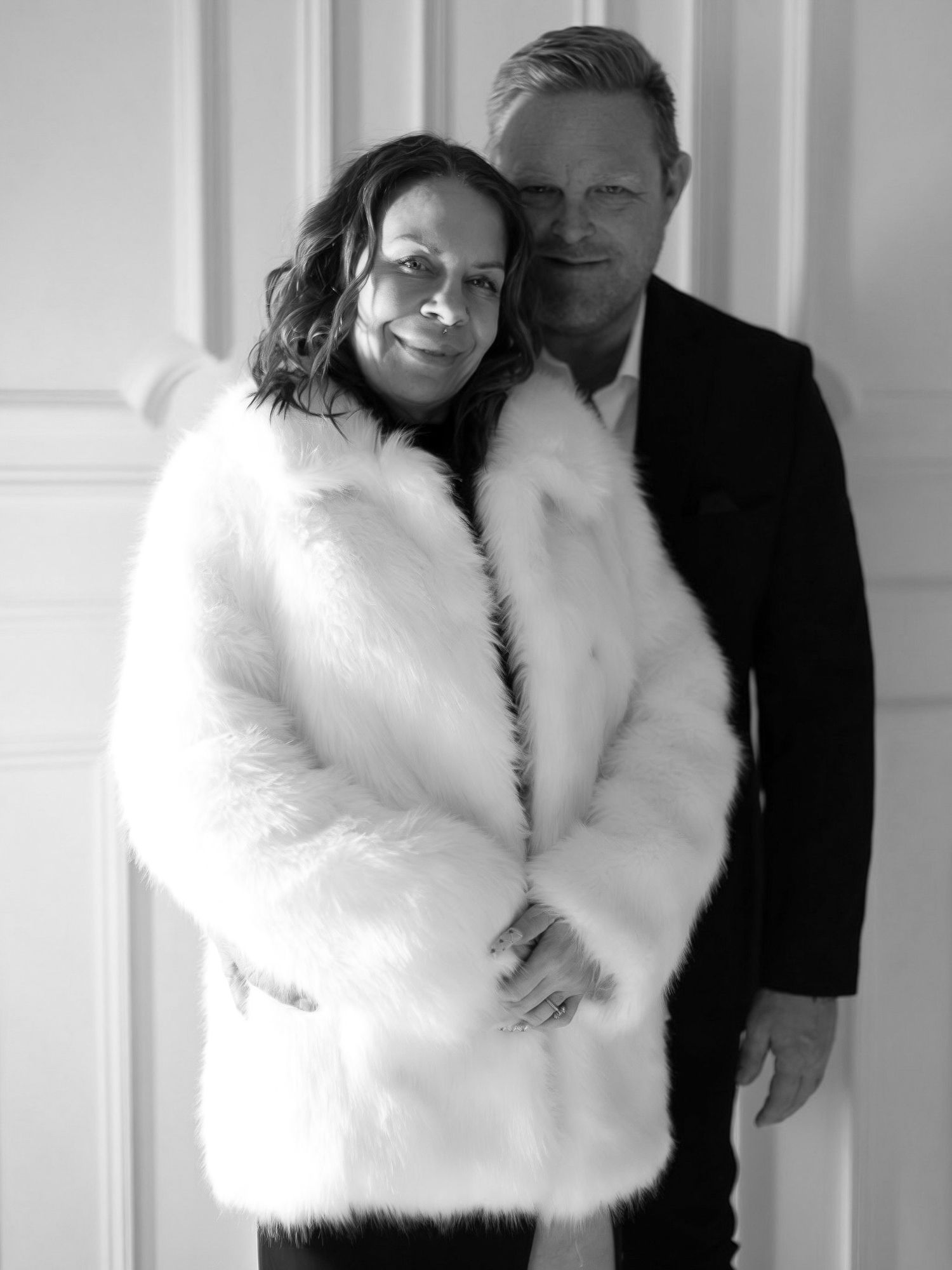 A black and white portrait of a couple posing together, with one wearing a luxurious white fur coat.