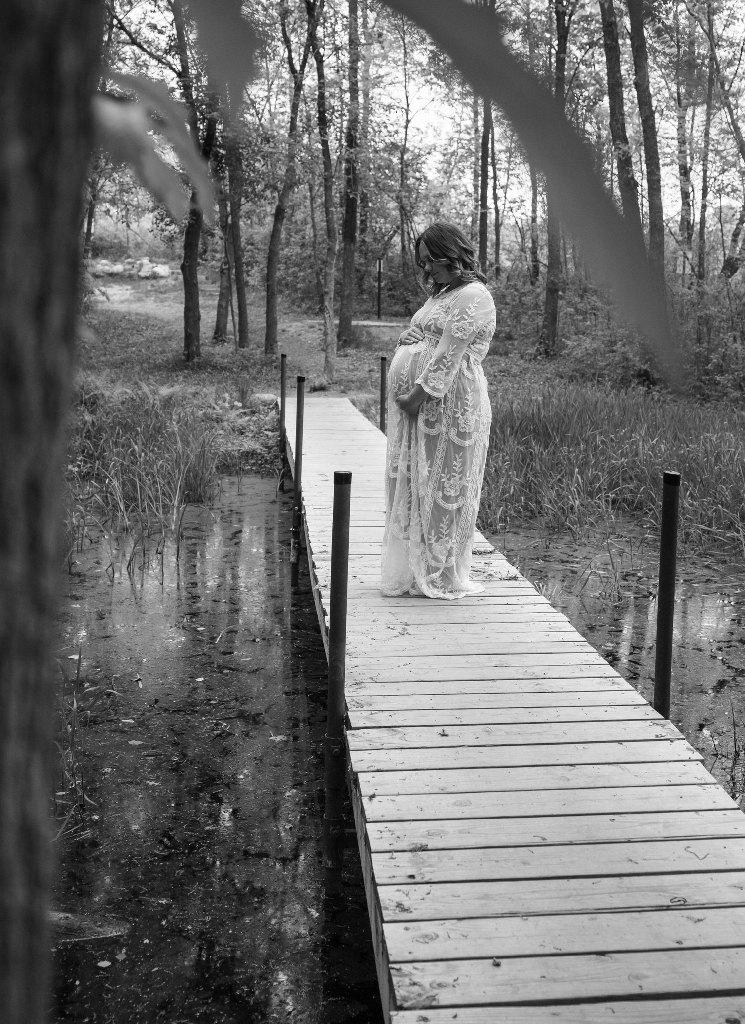 A figure in a flowing white dress stands on a wooden dock over still waters in a misty forest setting.