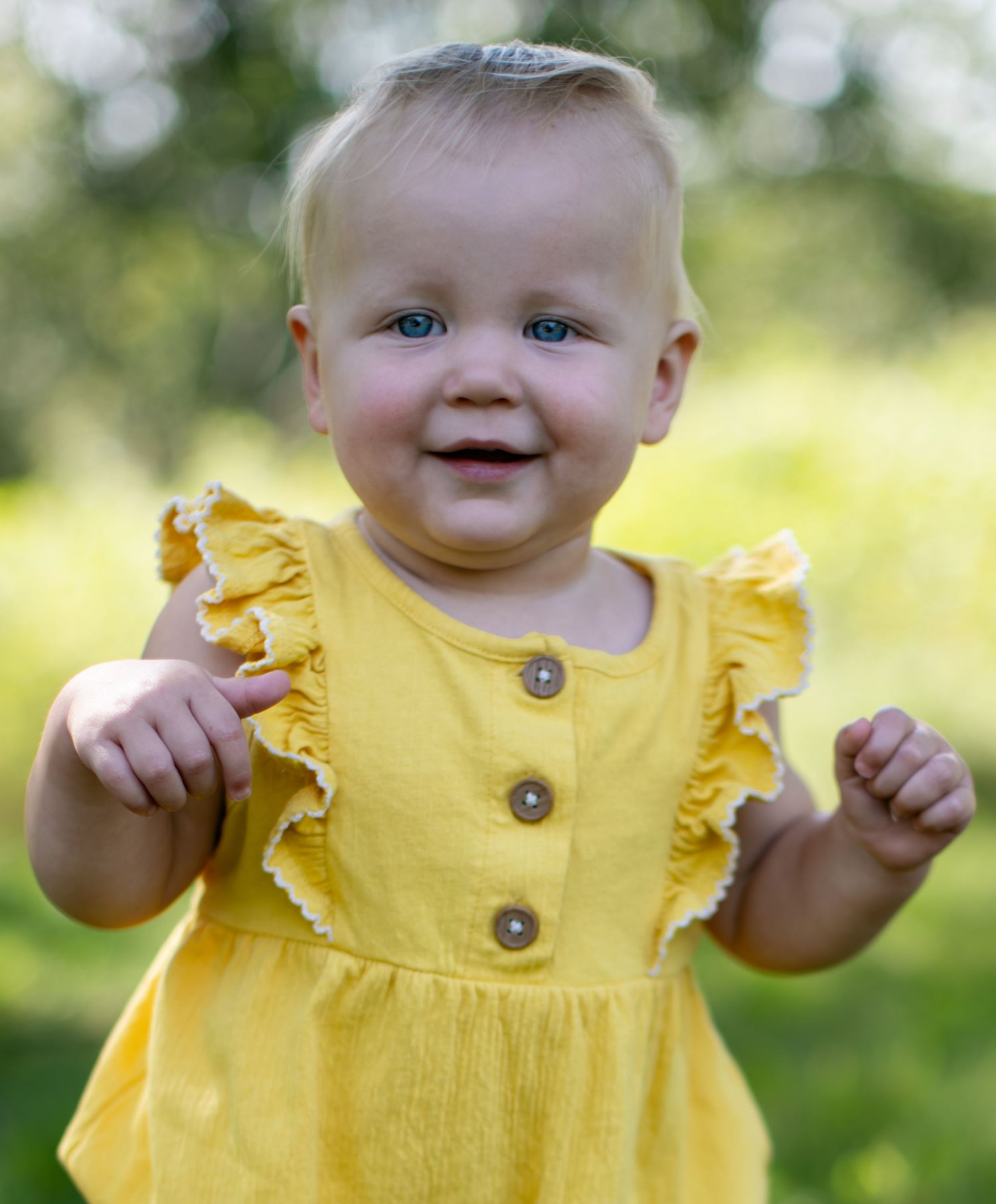 Baby in bright yellow ruffled dress outdoors in summer sunlight.