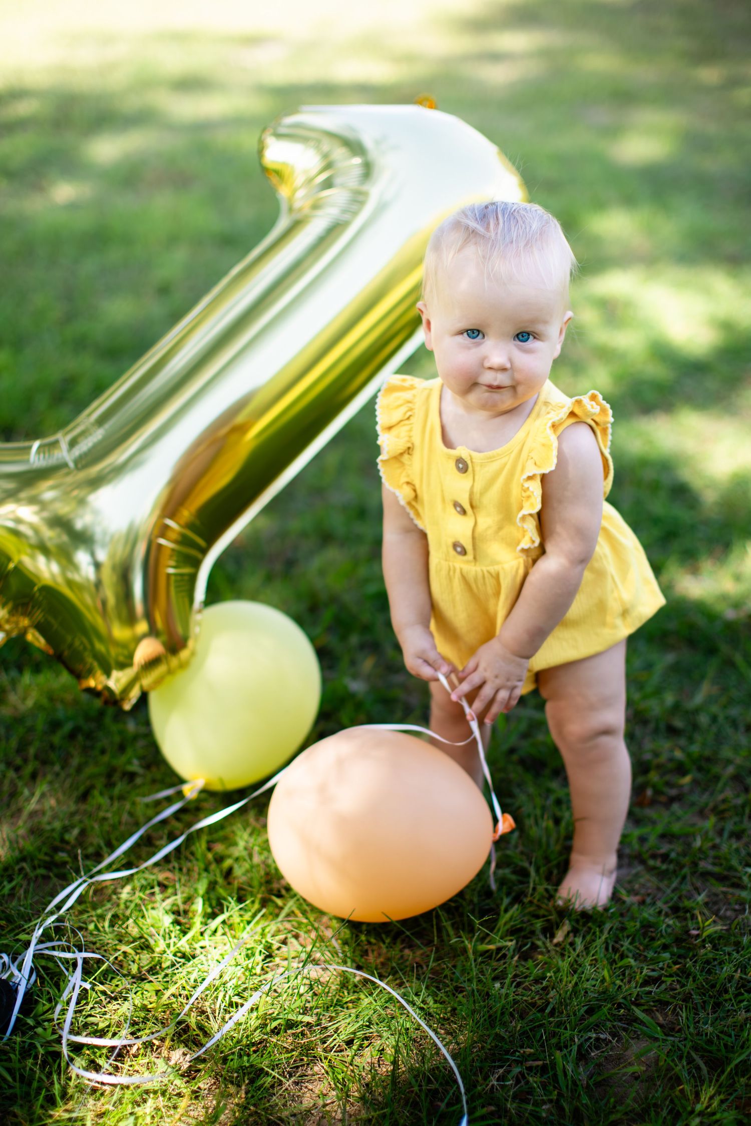 Baby crawling on grass with gold number one balloon and colorful party decorations.