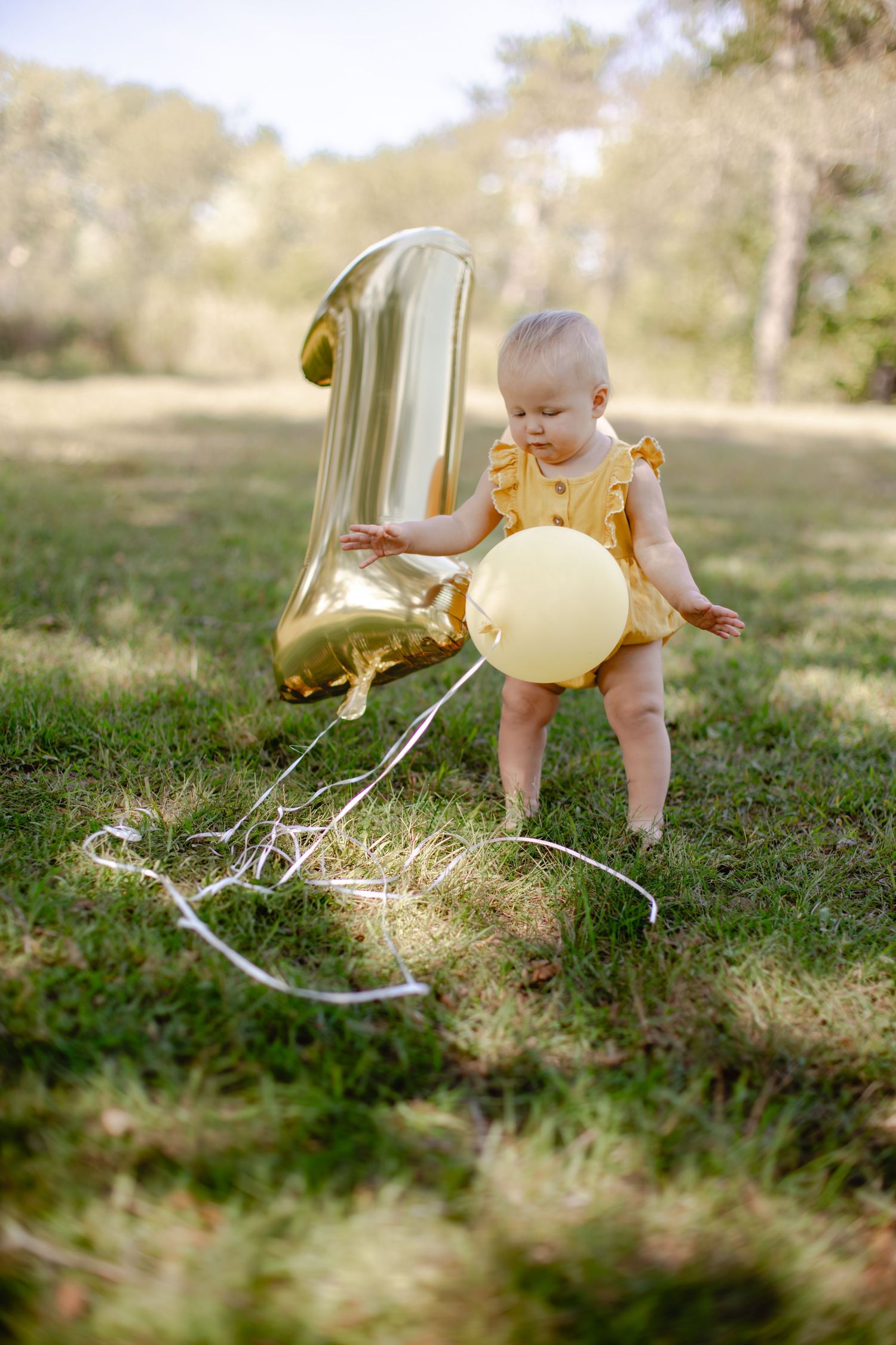 A child in a yellow dress explores and plays on grassy ground in soft natural lighting.